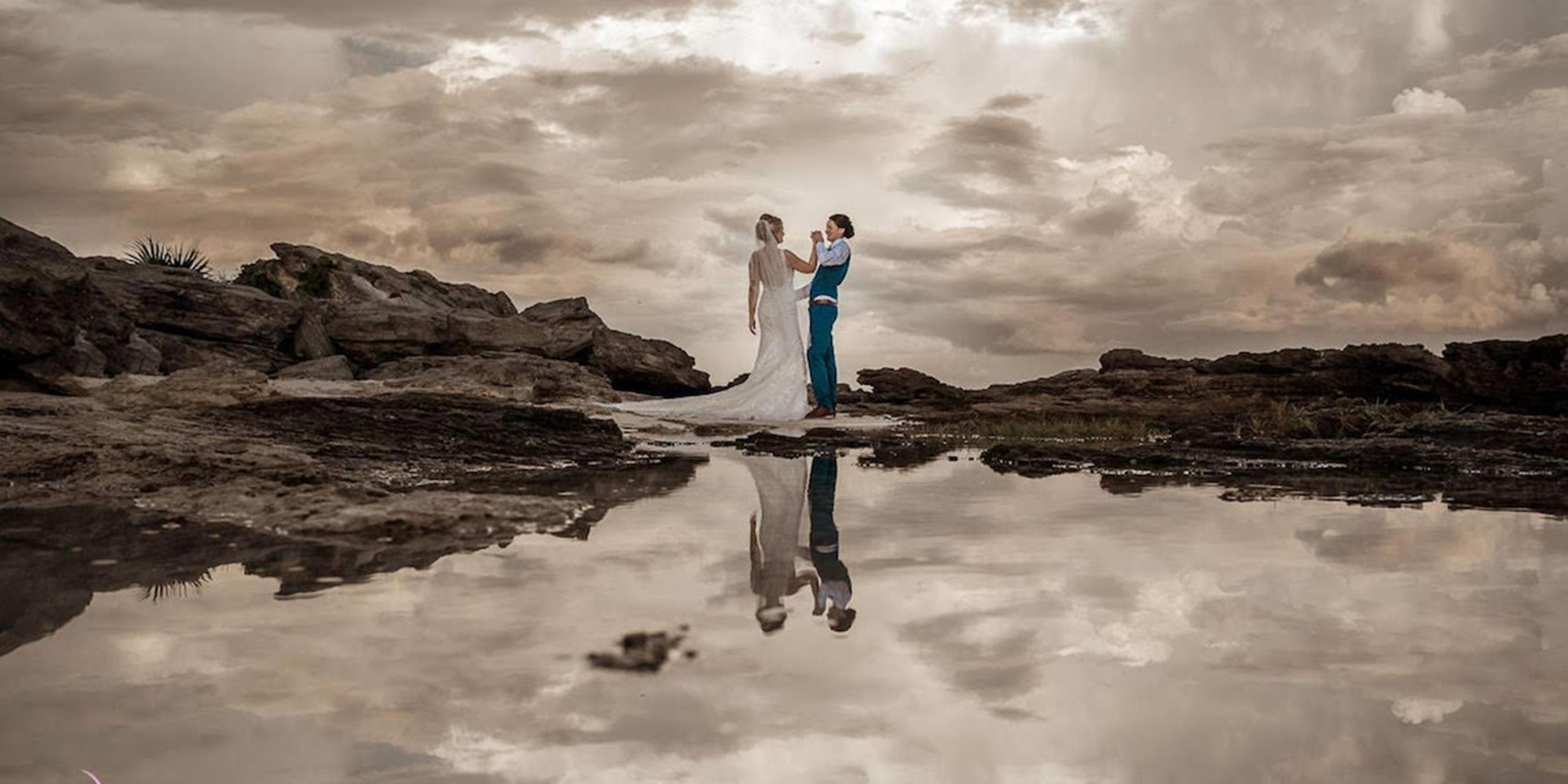 Tiana and Jessica post on the rocky beach at their dream destination wedding by Destify