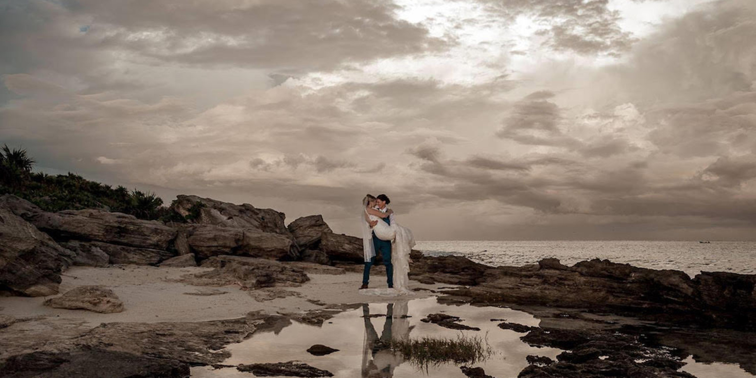 Tiana and Jessica post on the rocky beach at their dream destination wedding by Destify