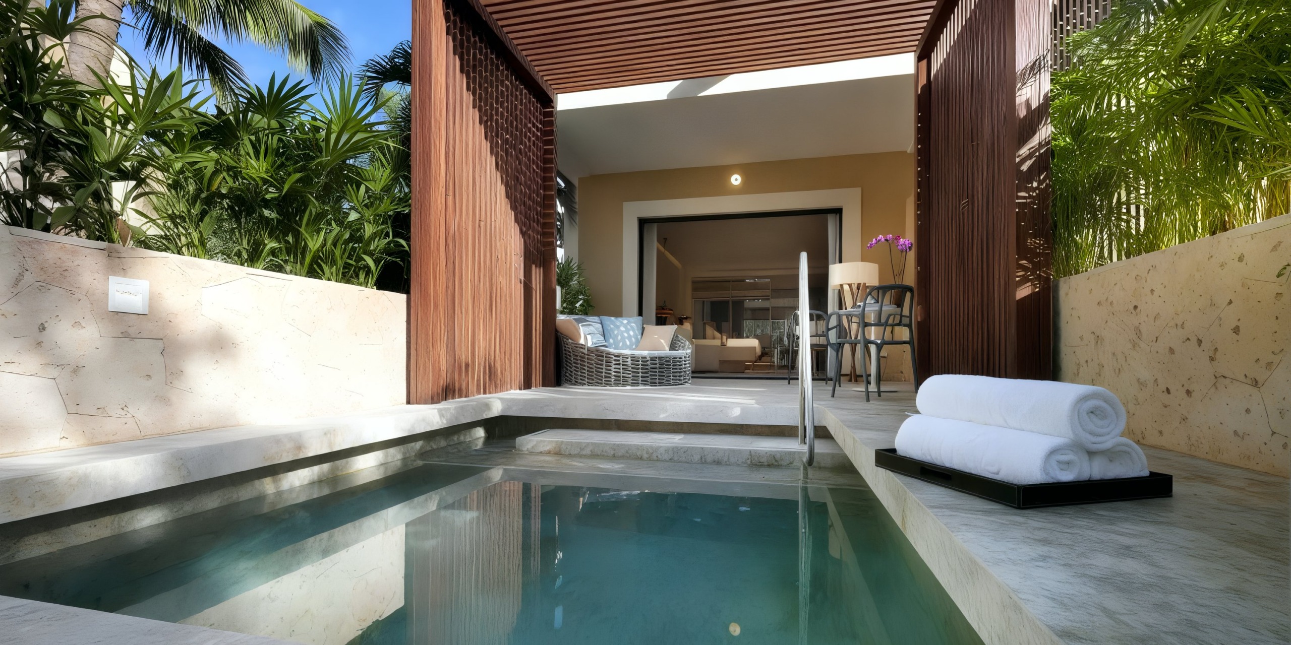 The TRS Yucatan features a small private pool surrounded by a tiled deck, leading to an outdoor seating area complete with chairs and a table. The serene setting is further enhanced by lush greenery and a wooden canopy.
