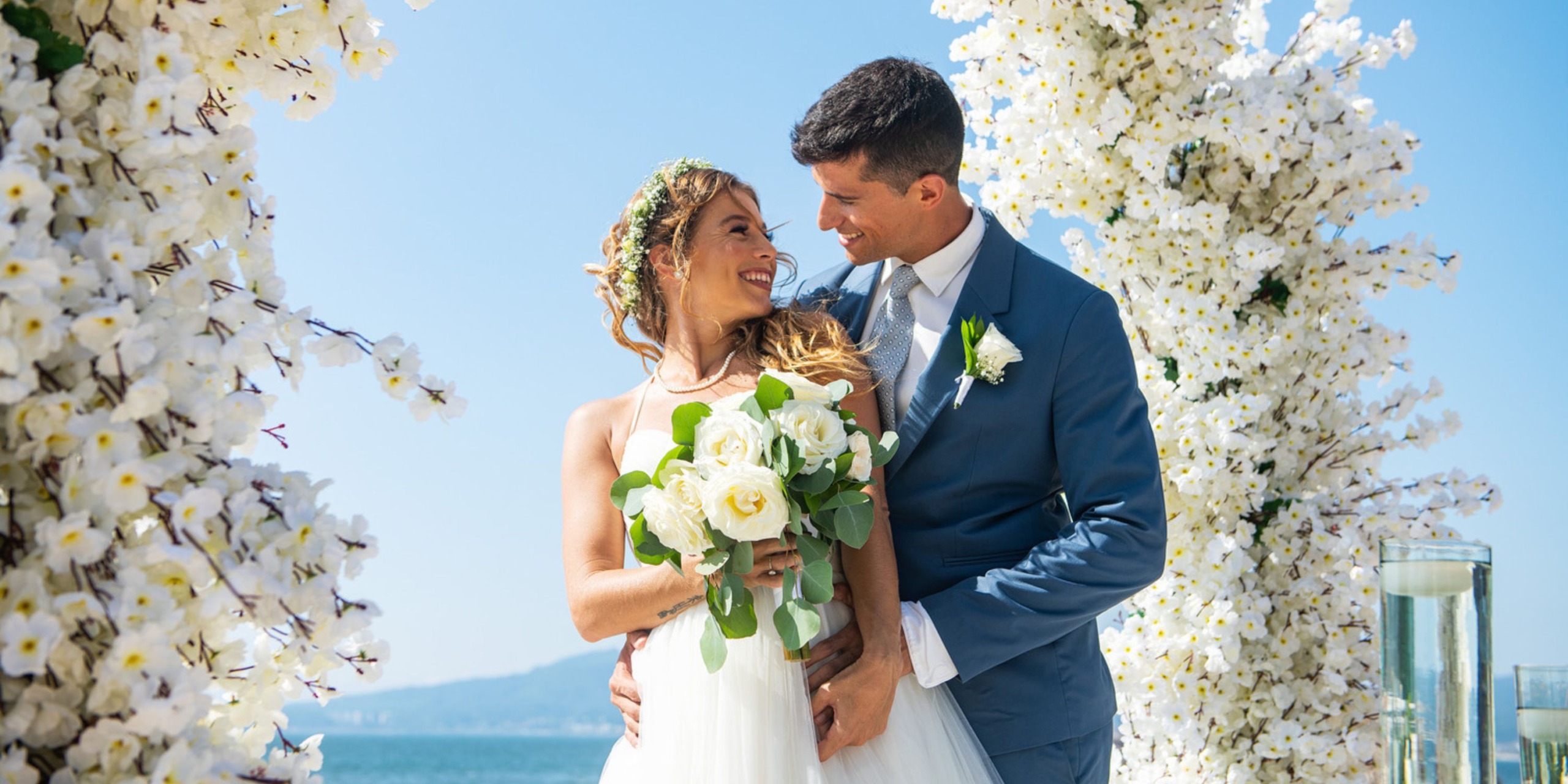 The bride and groom share a smile at their outdoor wedding at Wyndham Alltra Vallarta, surrounded by elegant white floral decor.