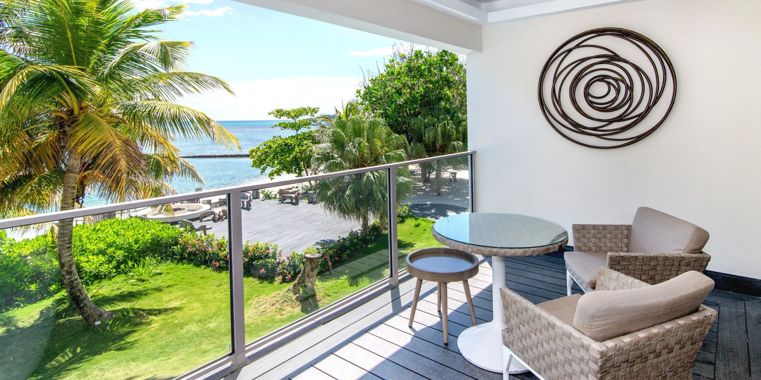 Enjoy a breathtaking balcony view from Zoetry Montego Bay, complete with two chairs and a table overlooking the beach. Savor the decor on the wall and admire the palm trees in sight.