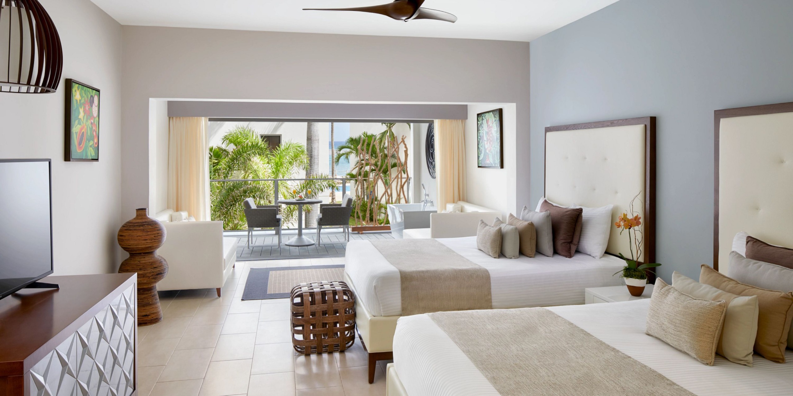 Experience the Zoetry Montego Bay with a hotel room featuring two comfortable beds, a ceiling fan, and a cozy sitting area. Enjoy the natural light pouring in through a large window that offers picturesque views of a balcony and lush greenery. The room is elegantly designed with a neutral color scheme to provide a serene atmosphere.