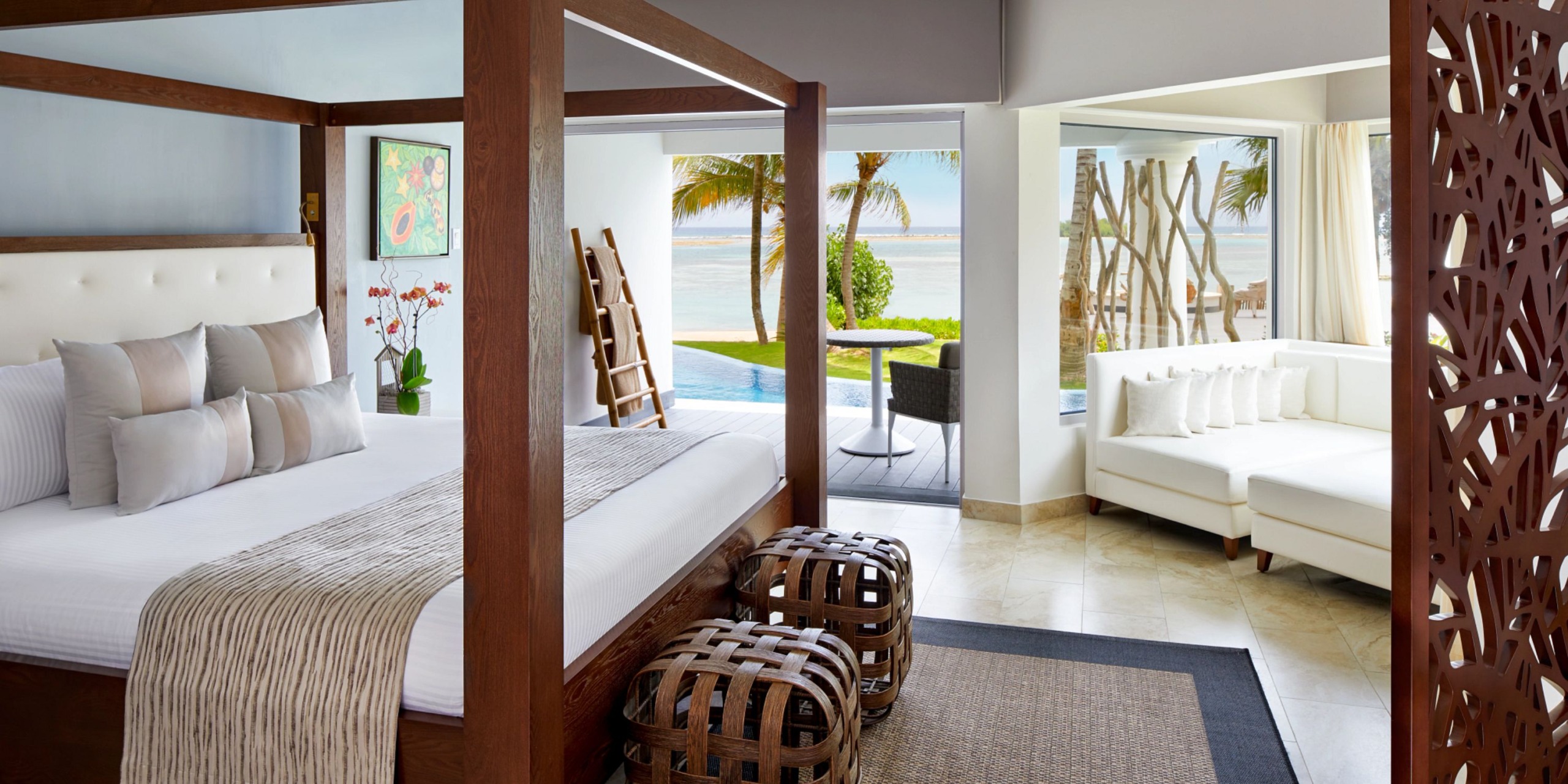 Experience the modern elegance of Zoetry Montego Bay, featuring a luxurious four-poster bed in a room with breathtaking ocean views and convenient patio access. The space is thoughtfully designed with comfortable seating, captivating wall art, and stylish decorative screen dividers.