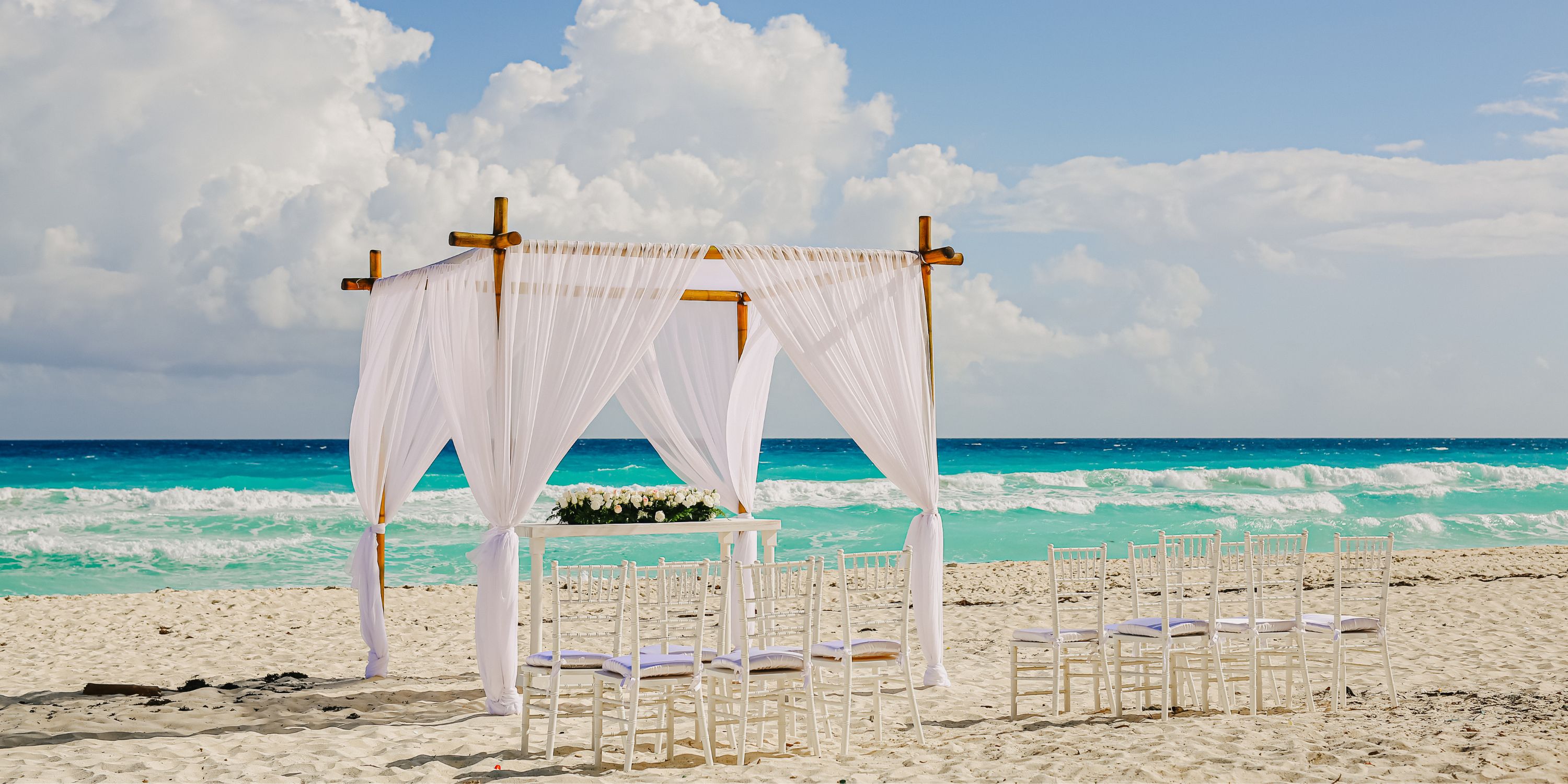 Destination wedding setup at Beach Palace Cancun with arch and chairs on sandy beach, turquoise ocean behind.