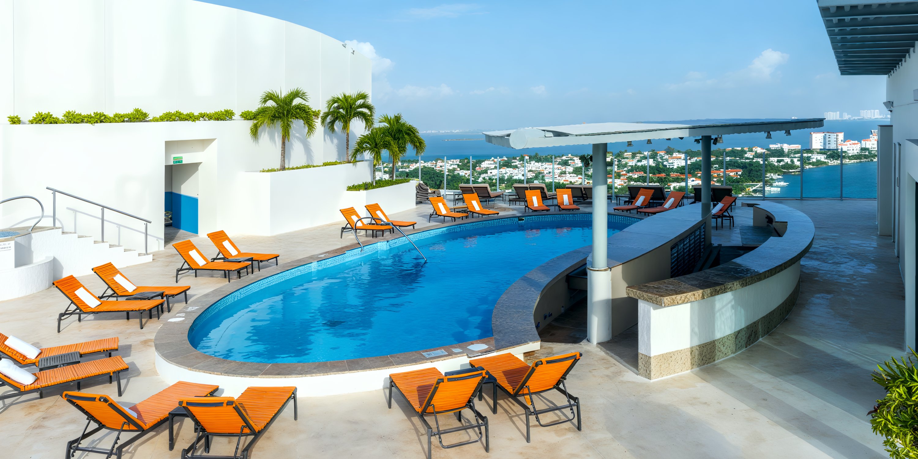 Beach Palace Cancun: The perfect destination wedding venue featuring a rooftop pool with stunning city views, set against a clear blue sky and surrounded by vibrant orange chairs.