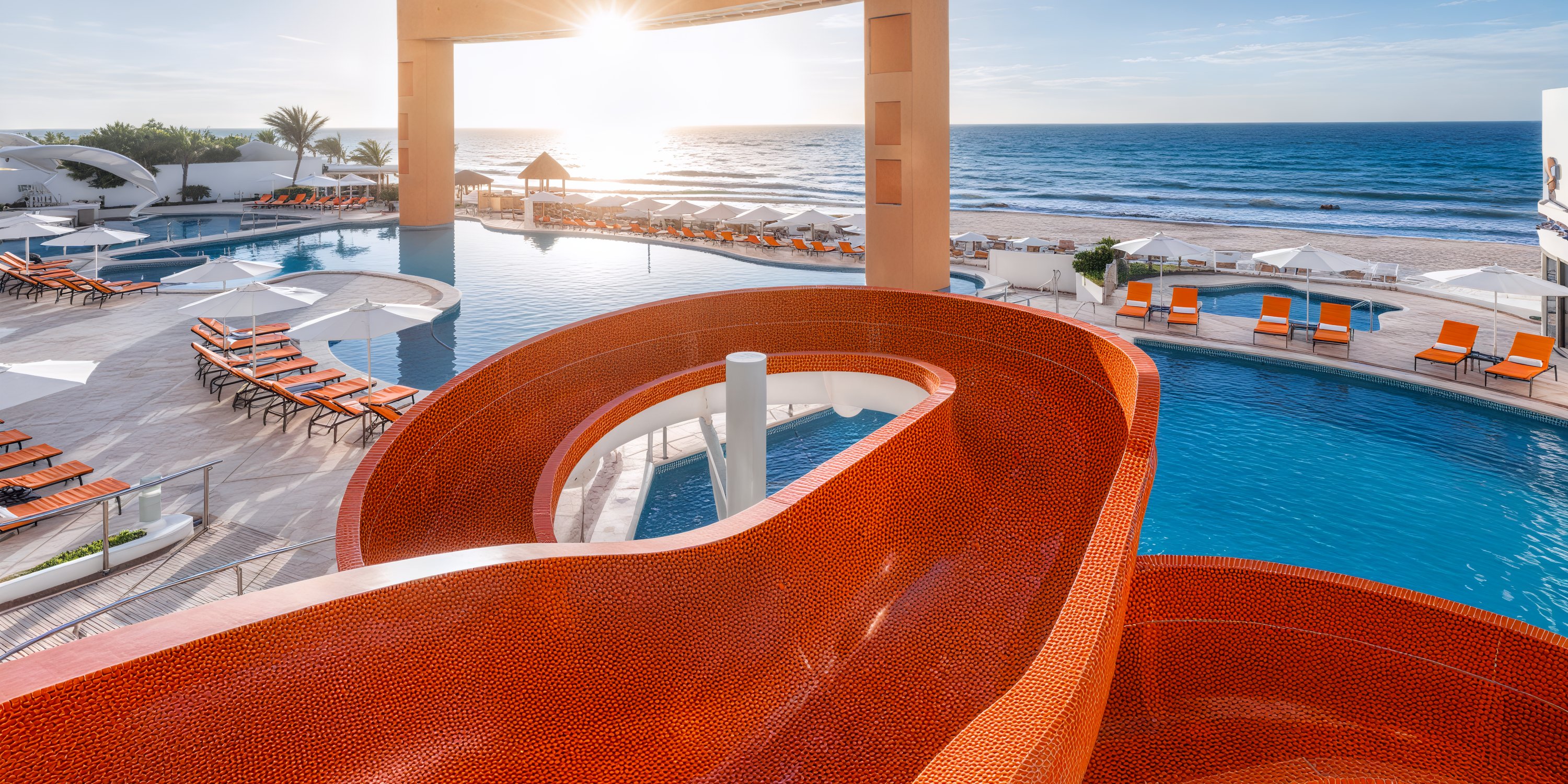 Beach Palace Cancun: A dreamy destination wedding location featuring a vibrant red waterslide beside the pool, breathtaking ocean views, and sun loungers perfectly positioned for a stunning sunrise.