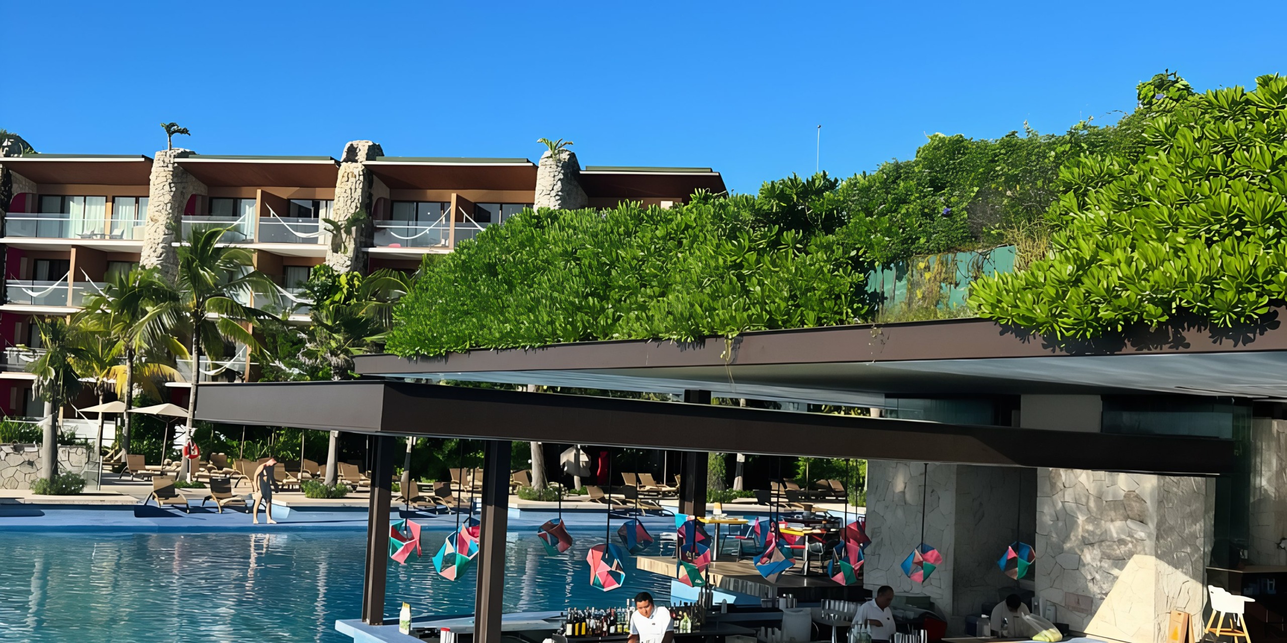 Luxury Hotel Xcaret pool area adorned with flags, surrounded by lush greenery and modern architecture under a clear blue sky.
