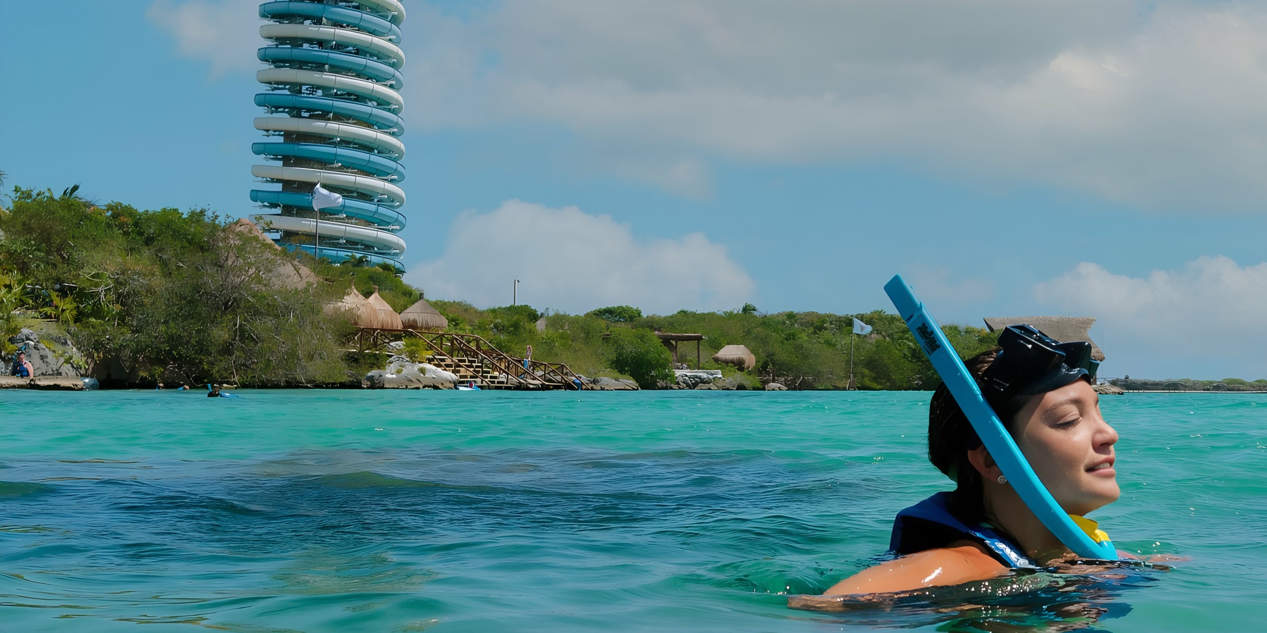 A woman snorkeling in clear water with Hotel Xcaret on a tropical coastline in the background.