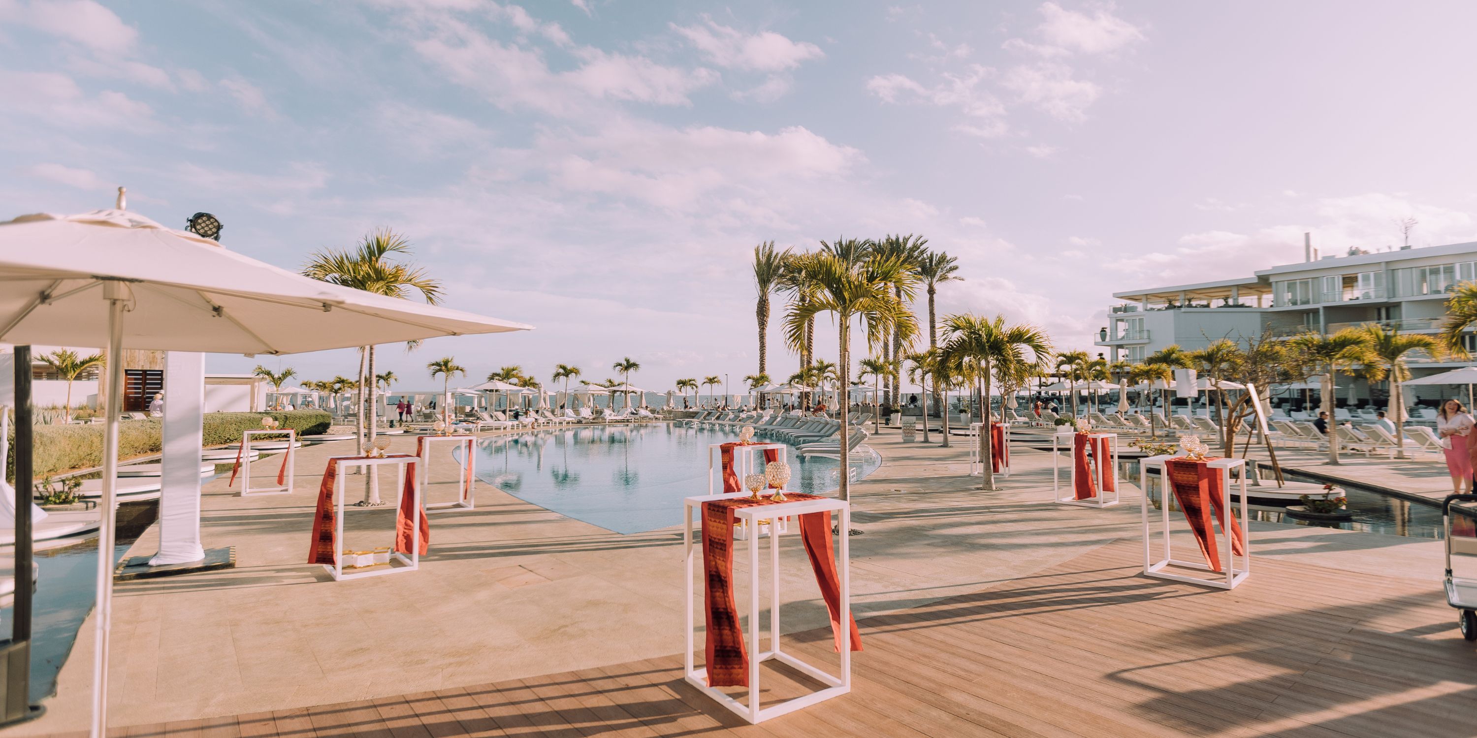 Poolside at Le Blanc Spa Resort Los Cabos: perfect for a destination wedding, with high tables, palm trees, lounge chairs, and a partly cloudy sky.