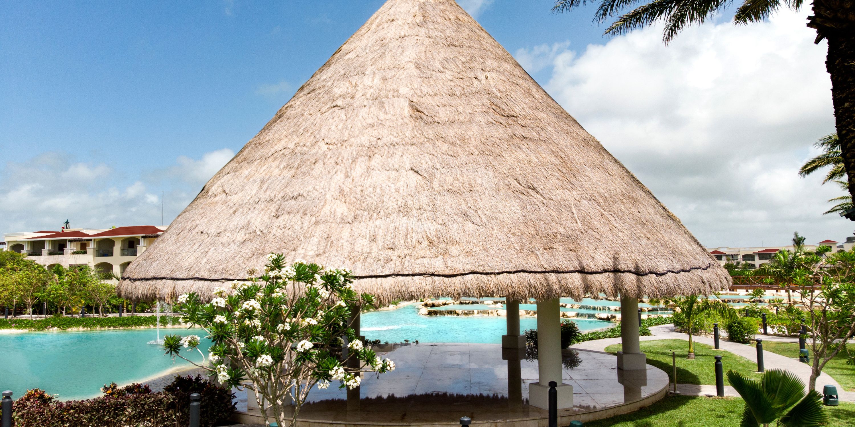 Thatched-roof gazebo at Moon Palace The Grand, perfect for a destination wedding, by the pool and palms.
