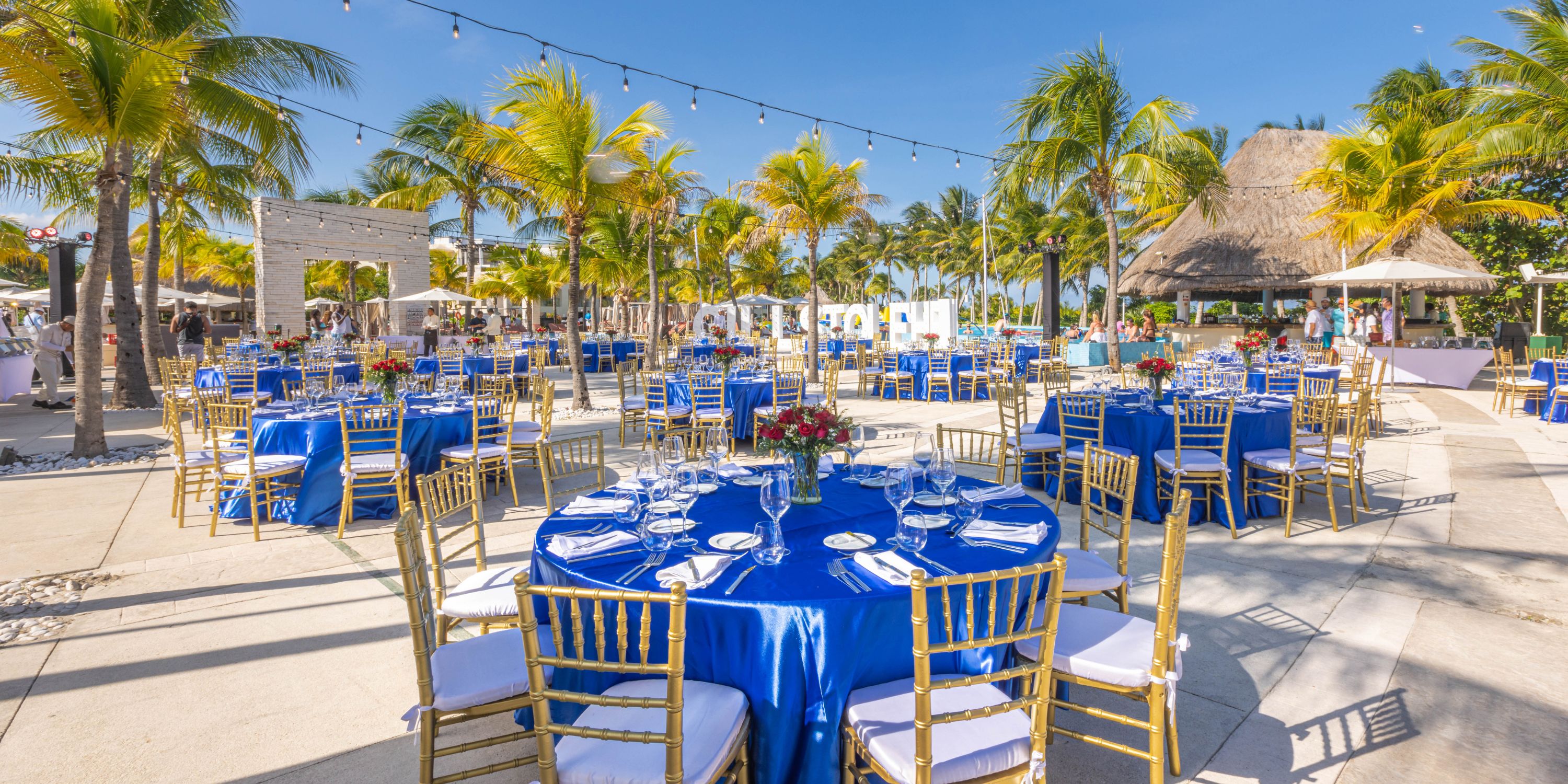 Destination wedding setup at Moon Palace The Grand with round tables, blue linens, and gold chairs under palms.