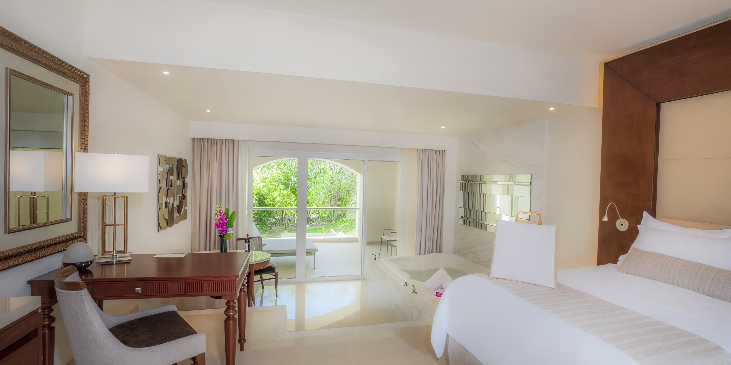 A spacious room at Moon Palace The Grand, adorned with a comfortable bed, desk, and luxurious bathtub, offers a picturesque garden view through its window—perfect for those attending a destination wedding.
