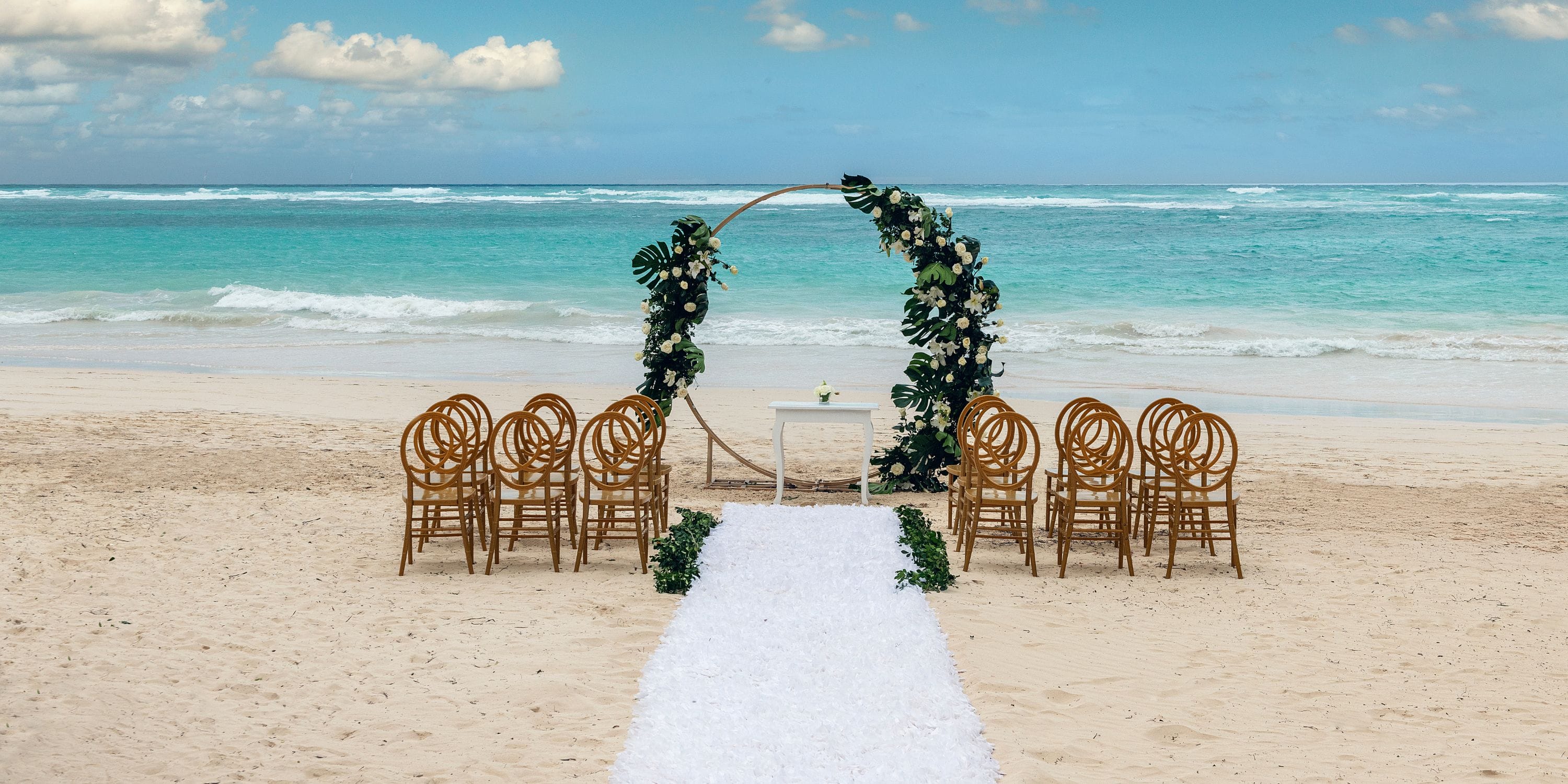 Rows of chairs face a floral arch and table at Ocean Blue and Sand for a destination wedding by the ocean.