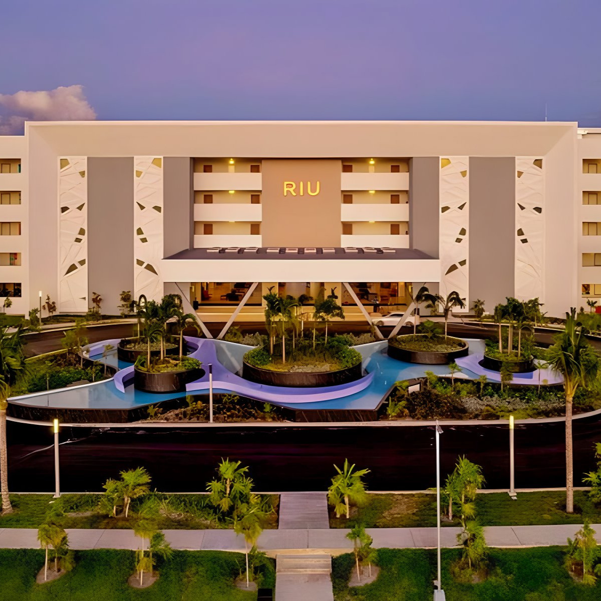 Aerial view of Hotel Riu Latino, a prime location for destination weddings, featuring symmetrical modern architecture and surrounded by lush gardens and water features at twilight.