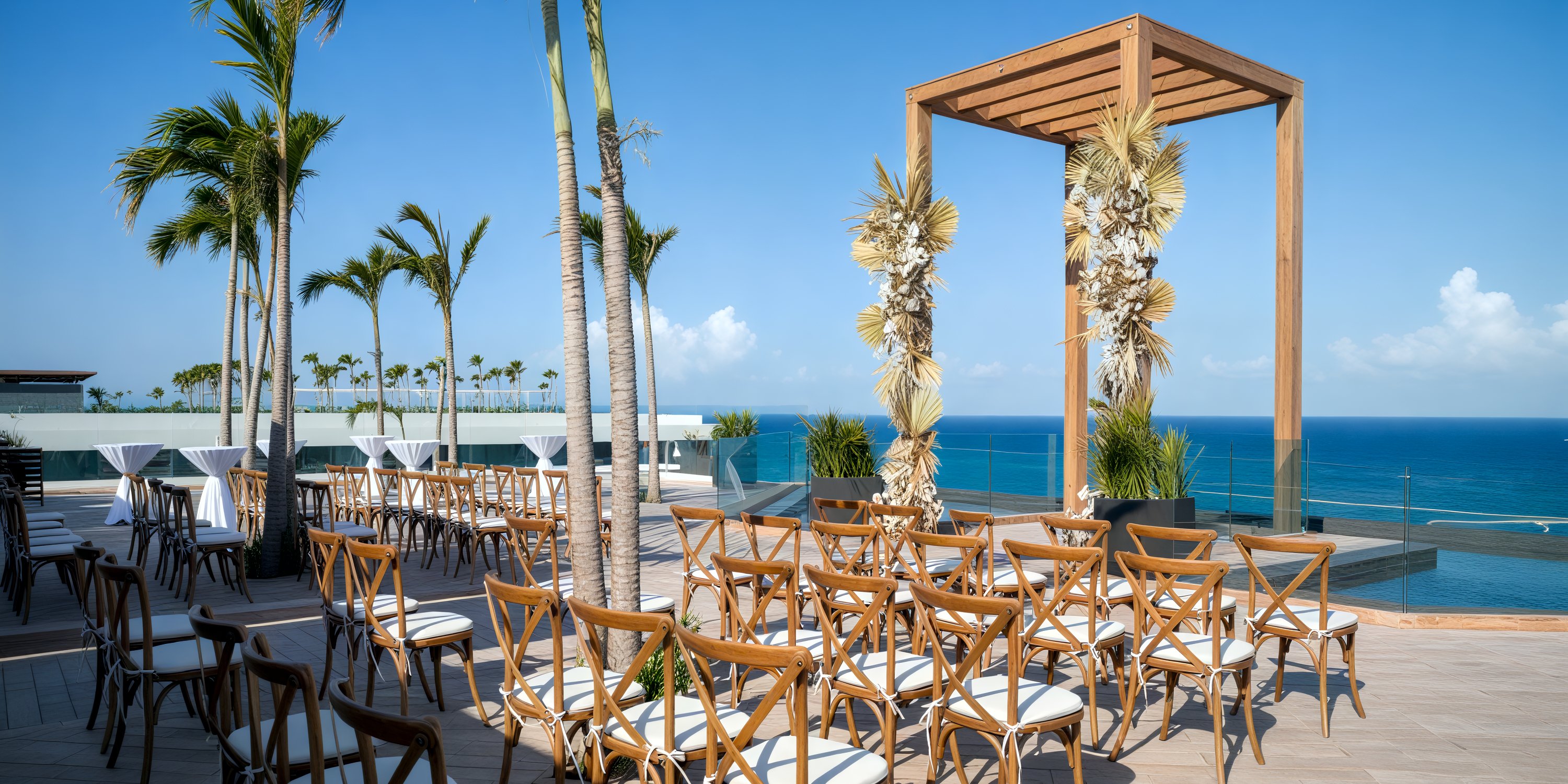 A picturesque destination wedding setup features wooden chairs arranged around a gazebo, all with a stunning view of the ocean.