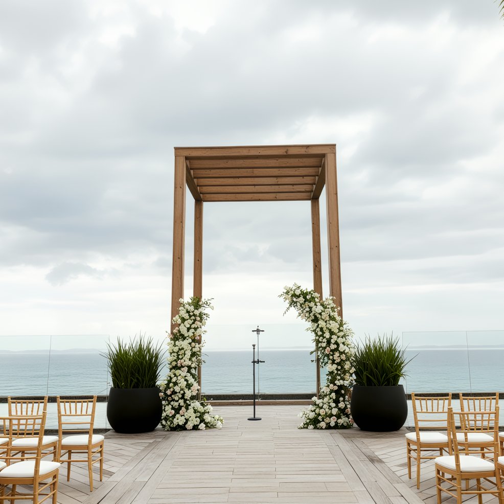 A destination wedding altar is beautifully arranged by the seaside, set beneath a canopy of cloudy skies.