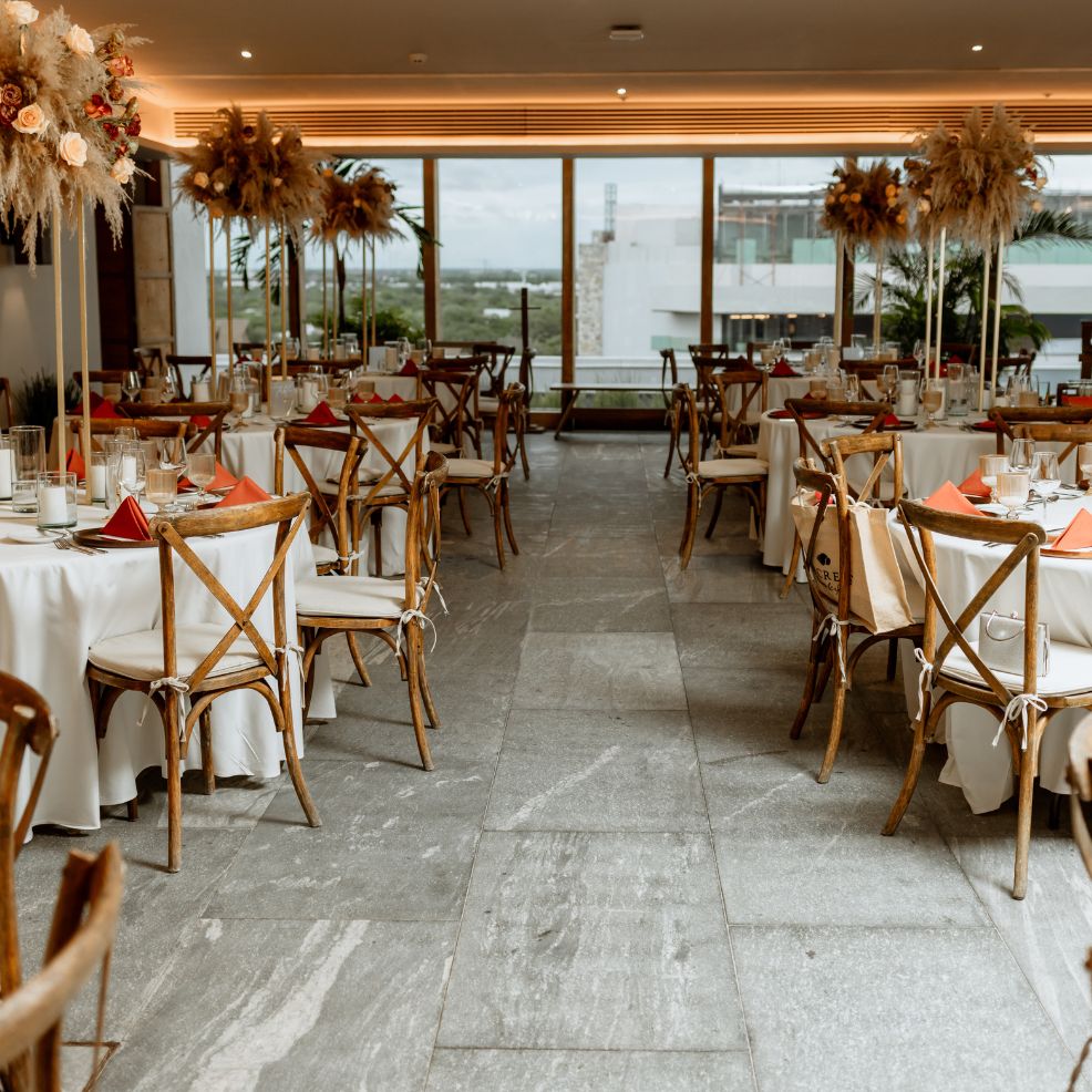 A decorated destination wedding banquet hall with round tables, wooden chairs, and large background windows.