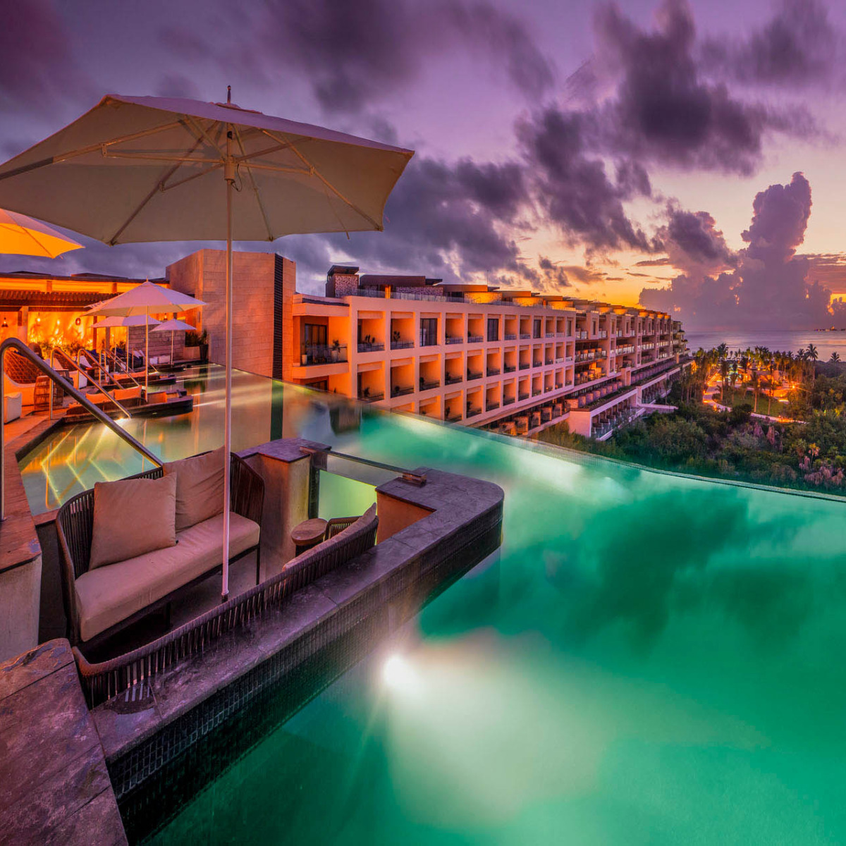Atelier Playa Mujeres, ideal for a destination wedding, with an infinity pool overlooking the ocean at sunset, featuring loungers and an umbrella.