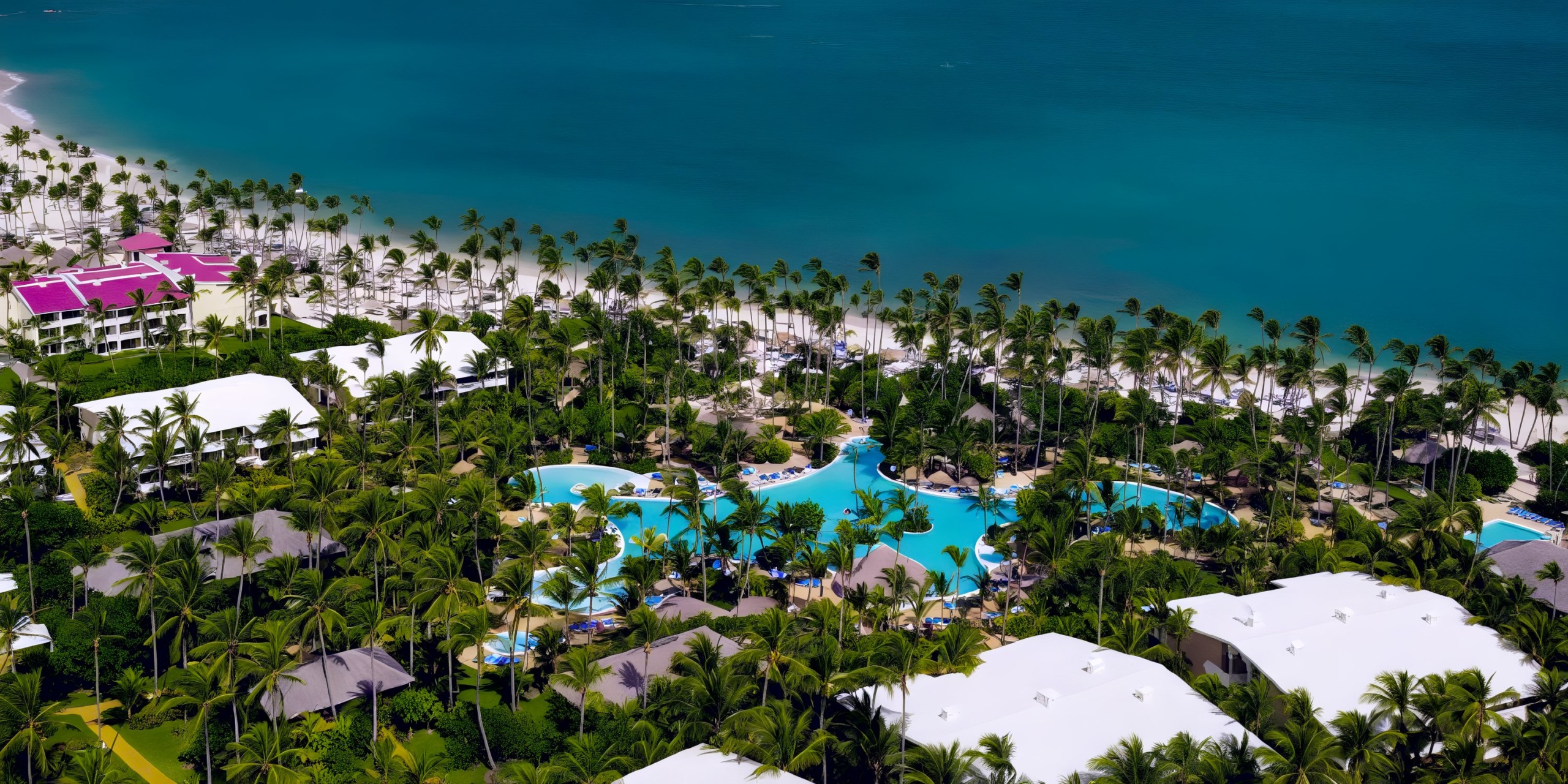 Aerial shot of Melia Punta Cana Beach, showcasing its white-roofed structures, expansive pool, palm trees, and pristine sandy beach by the turquoise ocean.