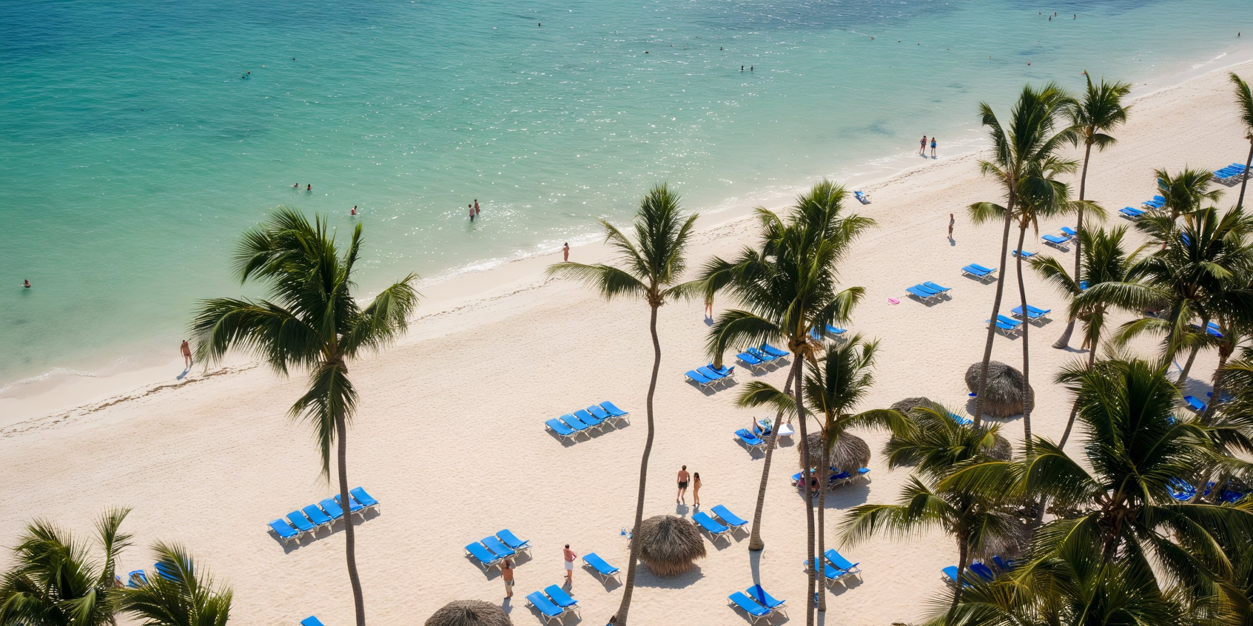Experience Melia Punta Cana Beach from above: a tropical paradise featuring palm trees, blue beach chairs, straw umbrellas, and visitors enjoying the sun-kissed sandy shore and sparkling turquoise waters.