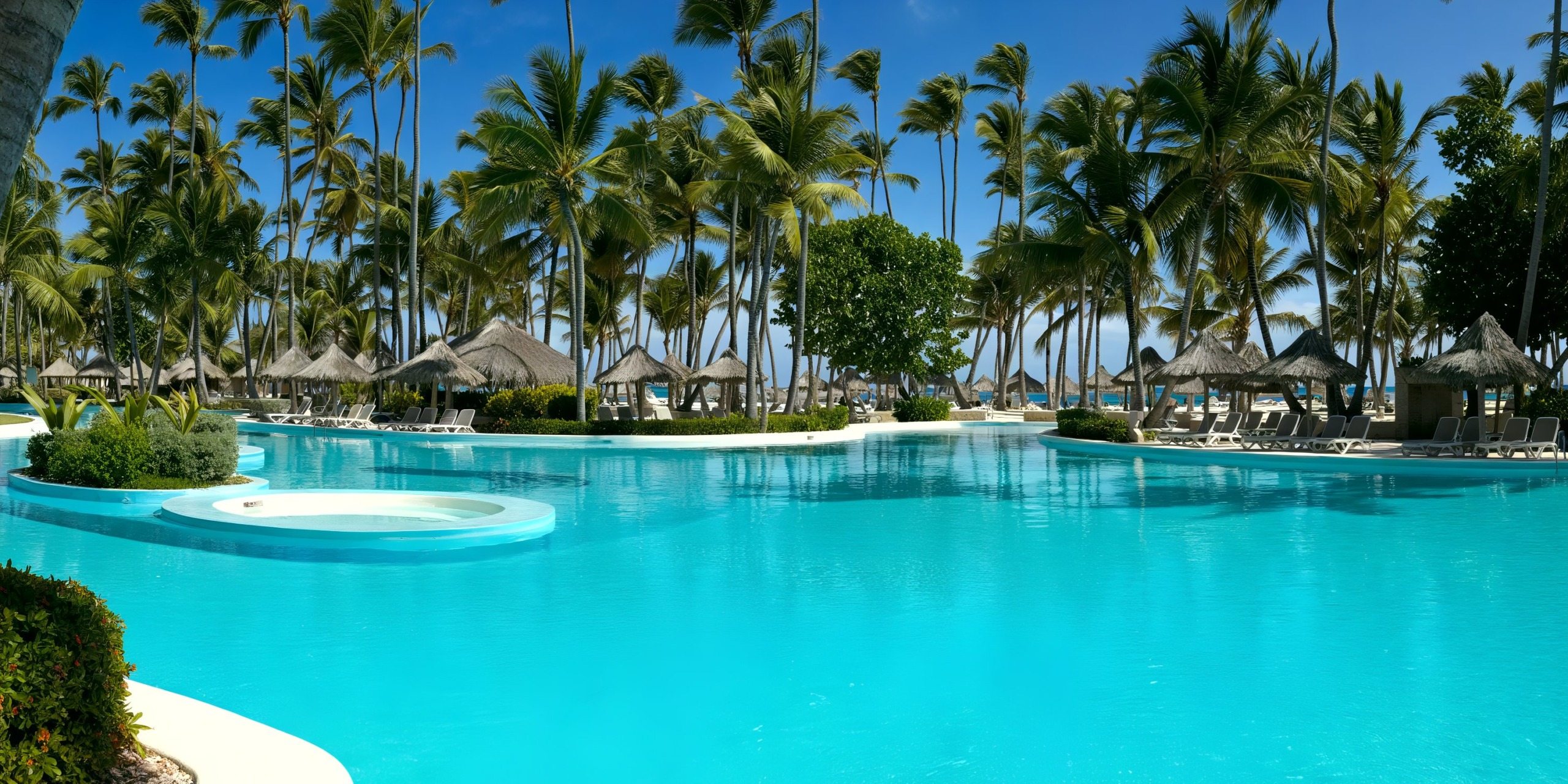 The Melia Punta Cana Beach features a spacious tropical swimming pool surrounded by palm trees, complemented by thatched umbrellas and deck chairs.