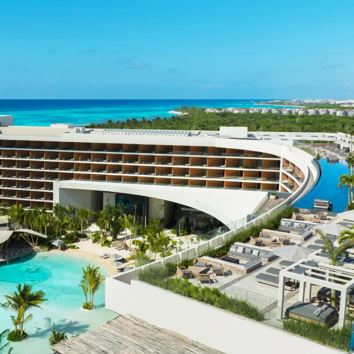 Luxurious Secrets Moxche beachfront hotel with a curved design, featuring balconies overlooking an expansive pool and the ocean in a tropical setting, perfect for a destination wedding.