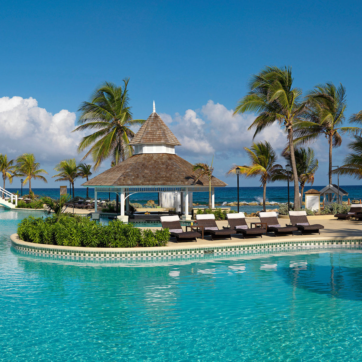 Luxury poolside lounge area with sunbeds and a central gazebo, perfect for a destination wedding, overlooking the ocean under a clear blue sky at Melia Braco Village.