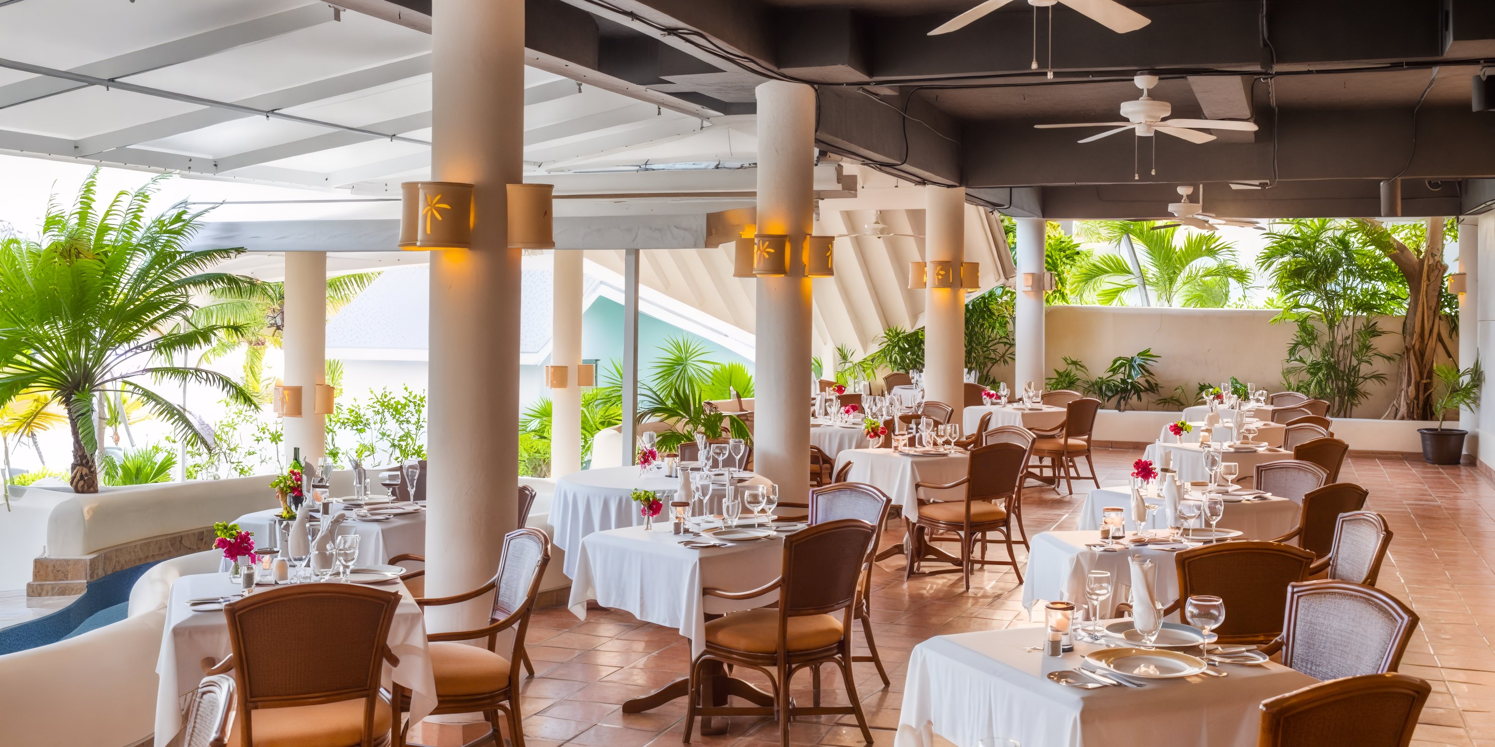 St. James's Club & Villas, Antigua: Experience the charm of open-air dining with wicker chairs and tables set amid lush plants, making it a perfect setting for an unforgettable destination wedding.