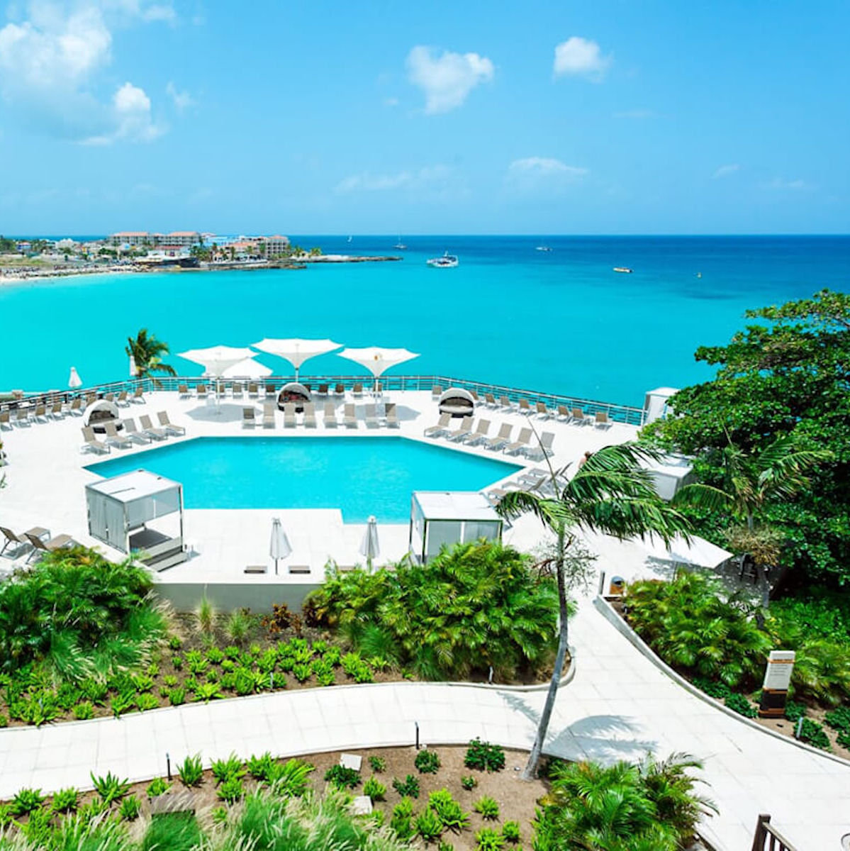 Aerial view of Sonesta Ocean Point pool overlooking a tropical beach with clear blue waters and boats, perfect for a destination wedding.