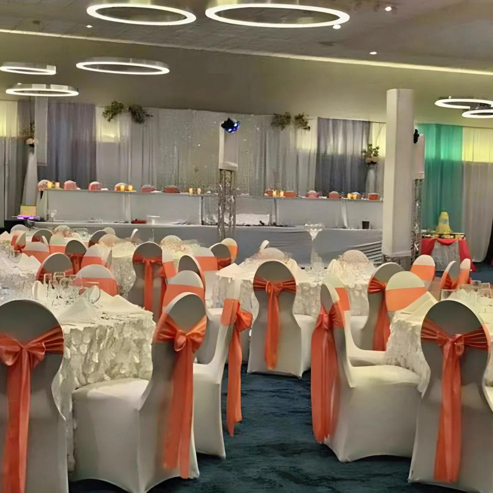 Elegantly decorated destination wedding reception hall with white-covered chairs accented with coral ribbons and tables set for a formal event.