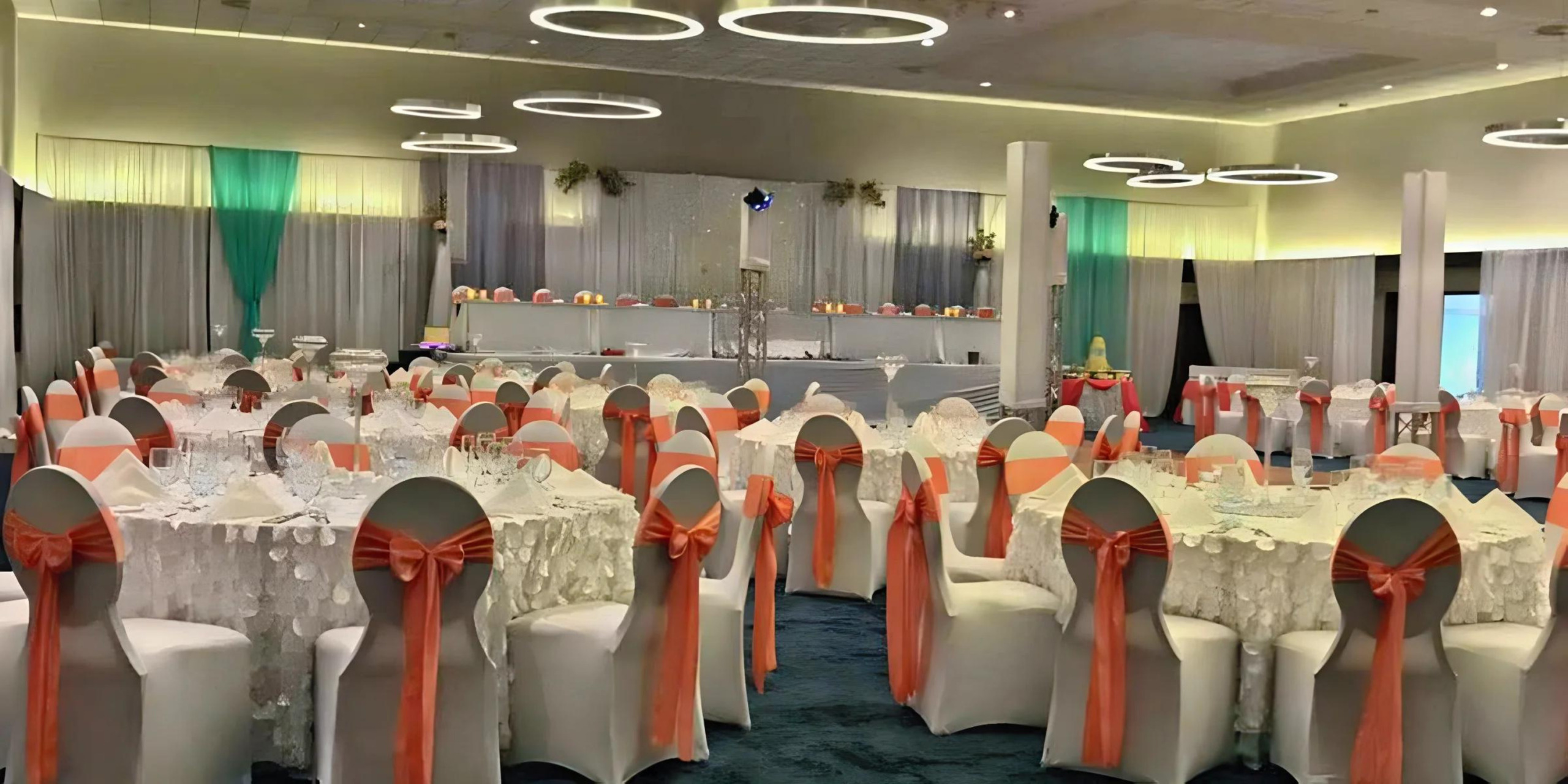 Elegant banquet hall decorated for destination weddings, with white-covered chairs featuring orange bows and tables set with fine dinnerware.