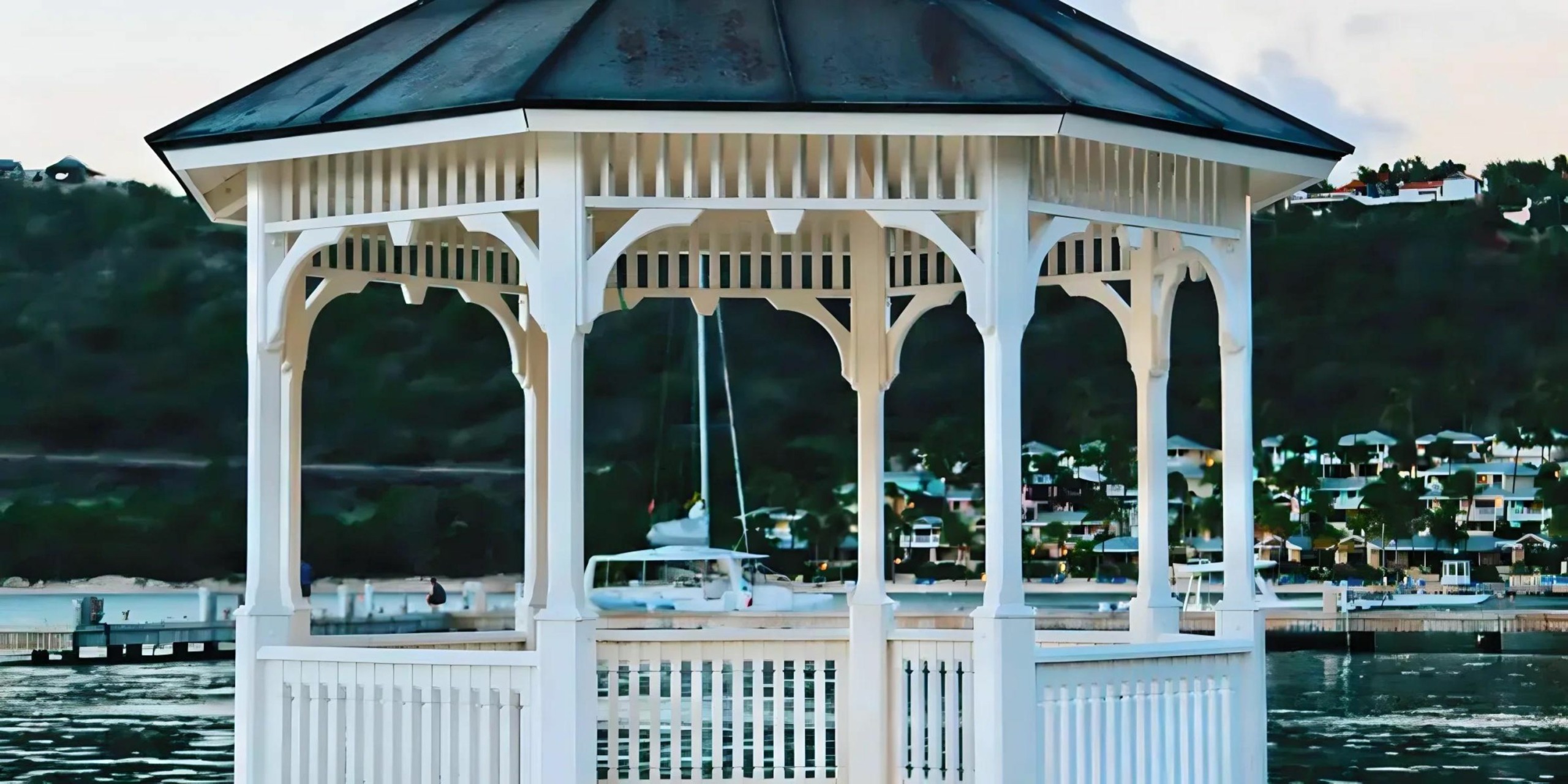 St. James's Club & Villas, Antigua on a pier, ideal for destination weddings, with a scenic backdrop of boats and green hills during twilight.