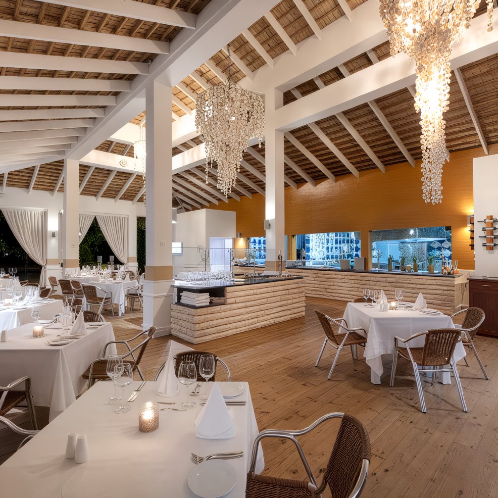 Sophisticated restaurant setting adorned with white tablecloths, wicker chairs, and decorative chandeliers, creating the perfect ambiance for a destination wedding celebration.