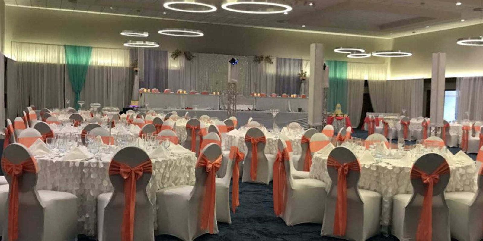 A Sonesta Maho Beach Resort wedding banquet hall with white tables and orange sashes.
