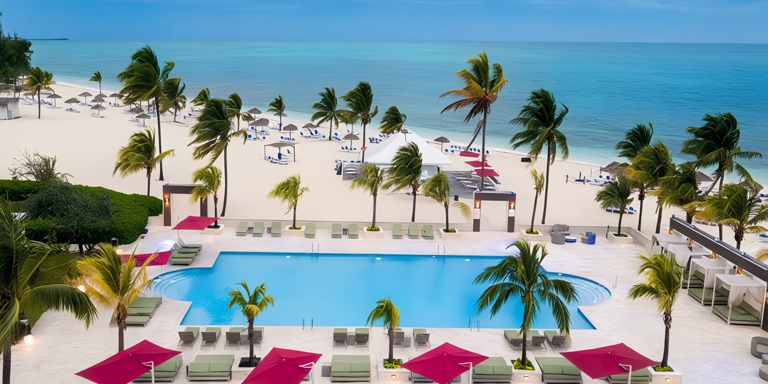 Aerial view of the Viva Wyndham Fortuna Beach resort featuring a pool, palm trees, loungers, and umbrellas by the ocean.
