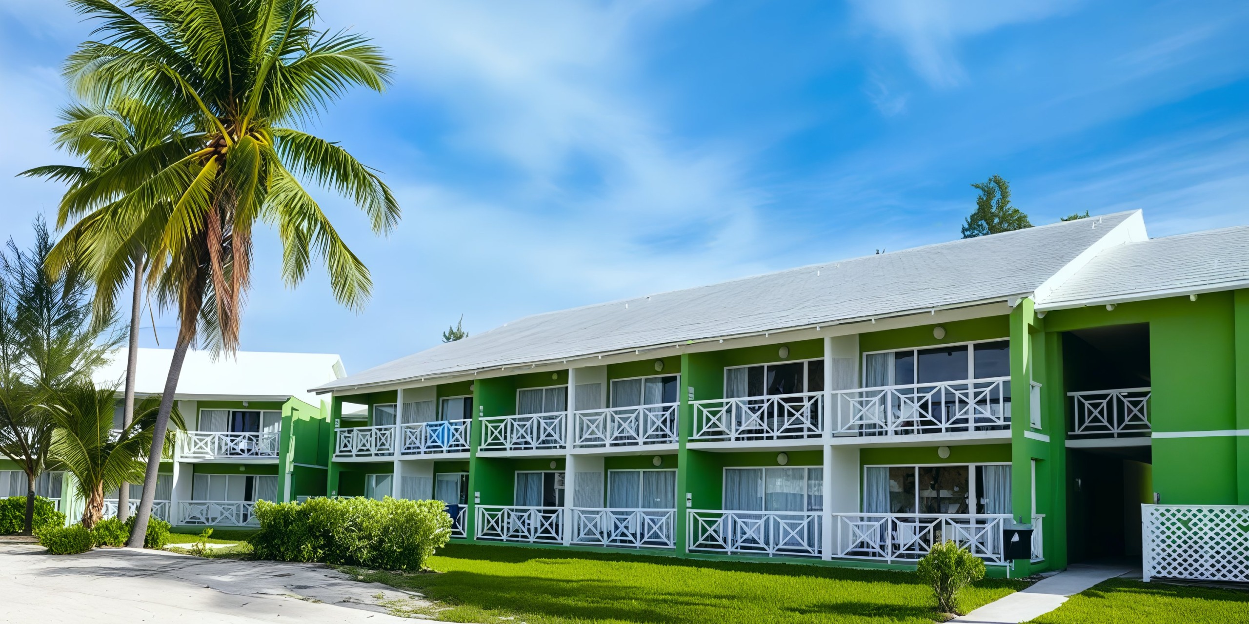 The Viva Wyndham Fortuna Beach hotel features a green building with white balconies and a palm tree in the foreground beneath a clear blue sky.