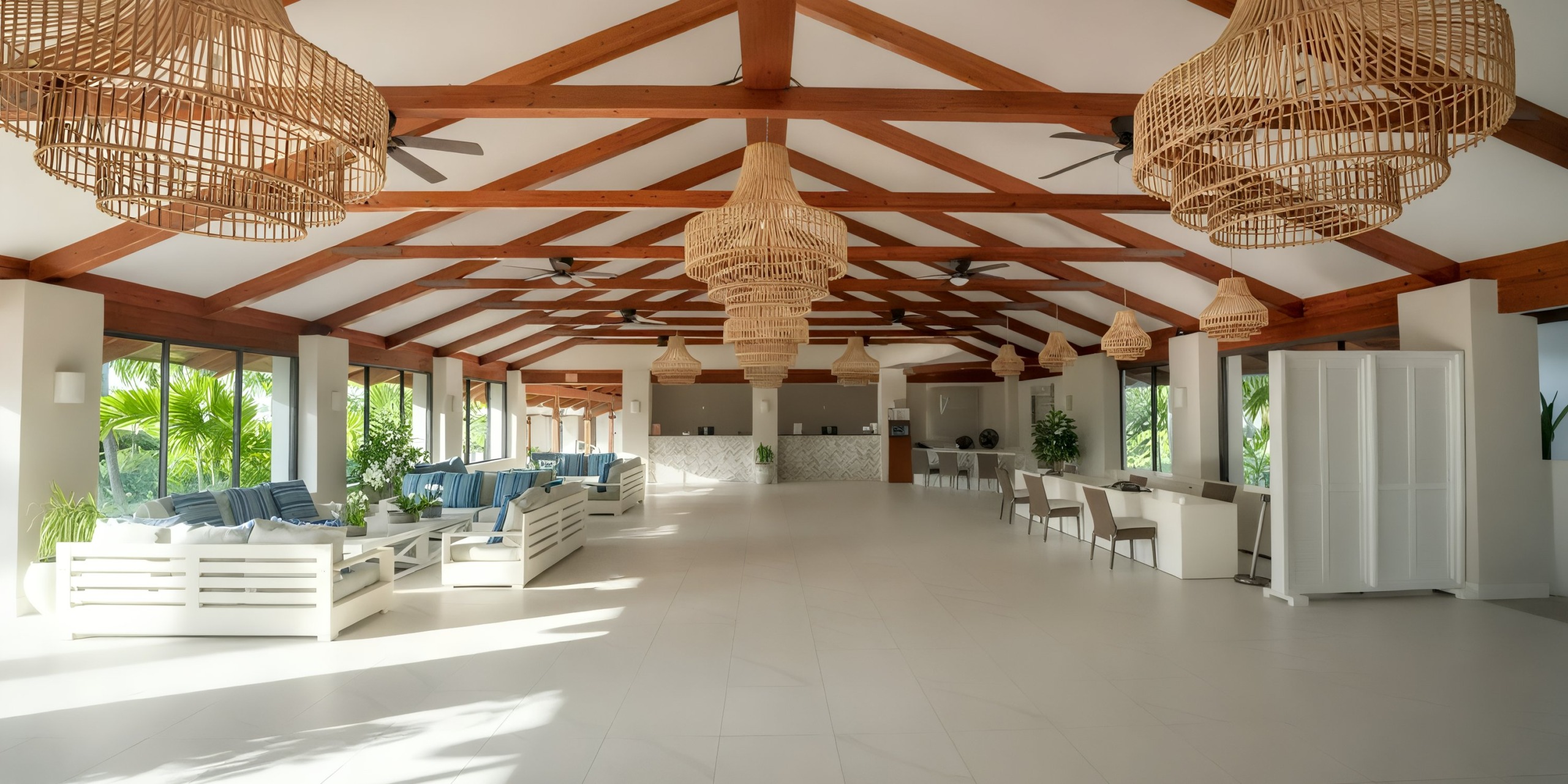 Enjoy a spacious open-concept room at Viva Wyndham Fortuna Beach, featuring wooden beams, wicker chandeliers, white sofas, and dining tables. Large windows allow natural light to illuminate the inviting space.