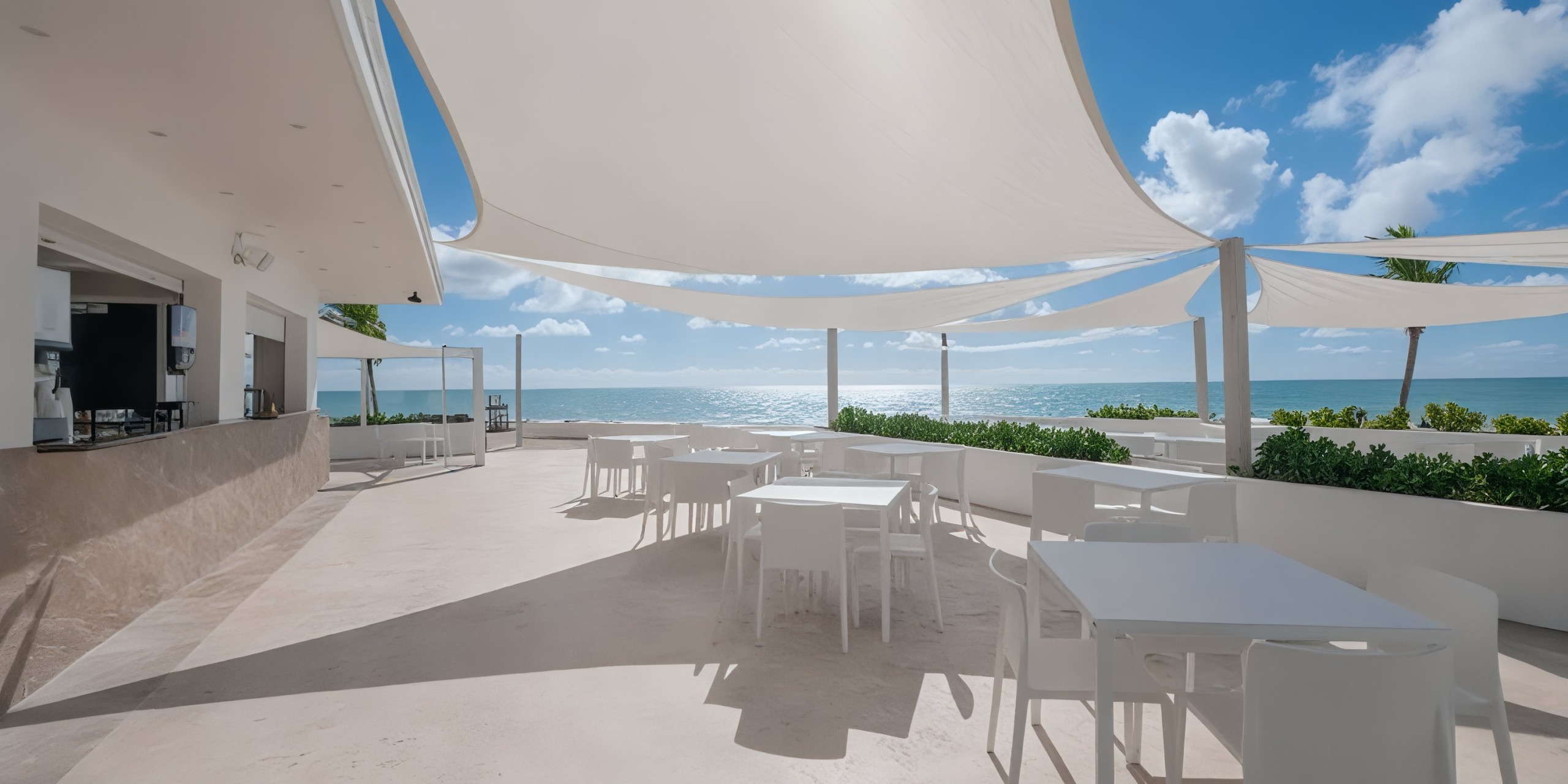 The outdoor patio at Viva Wyndham Fortuna Beach features white tables and chairs under large sun shades, offering a stunning view of the ocean on a sunny day.