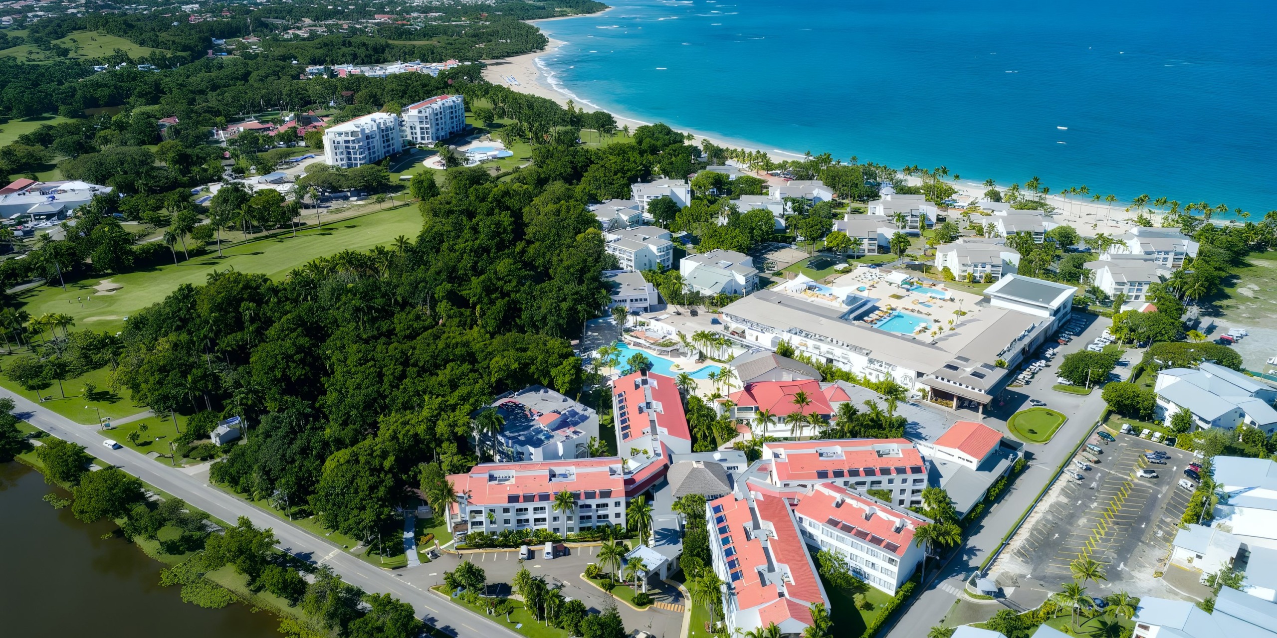Aerial view of Viva Wyndham V Heavens - All-Inclusive Resort, Adults Only, featuring red-roofed buildings, lush greenery, and a sandy beach along the turquoise ocean.