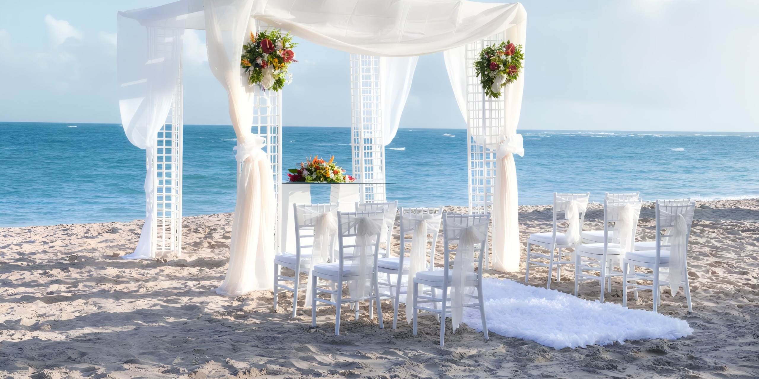 A beachfront wedding setup at Viva Wyndham V Heavens - All-Inclusive Resort, Adults Only, featuring white chairs and a flower-adorned canopy with stunning ocean views.
