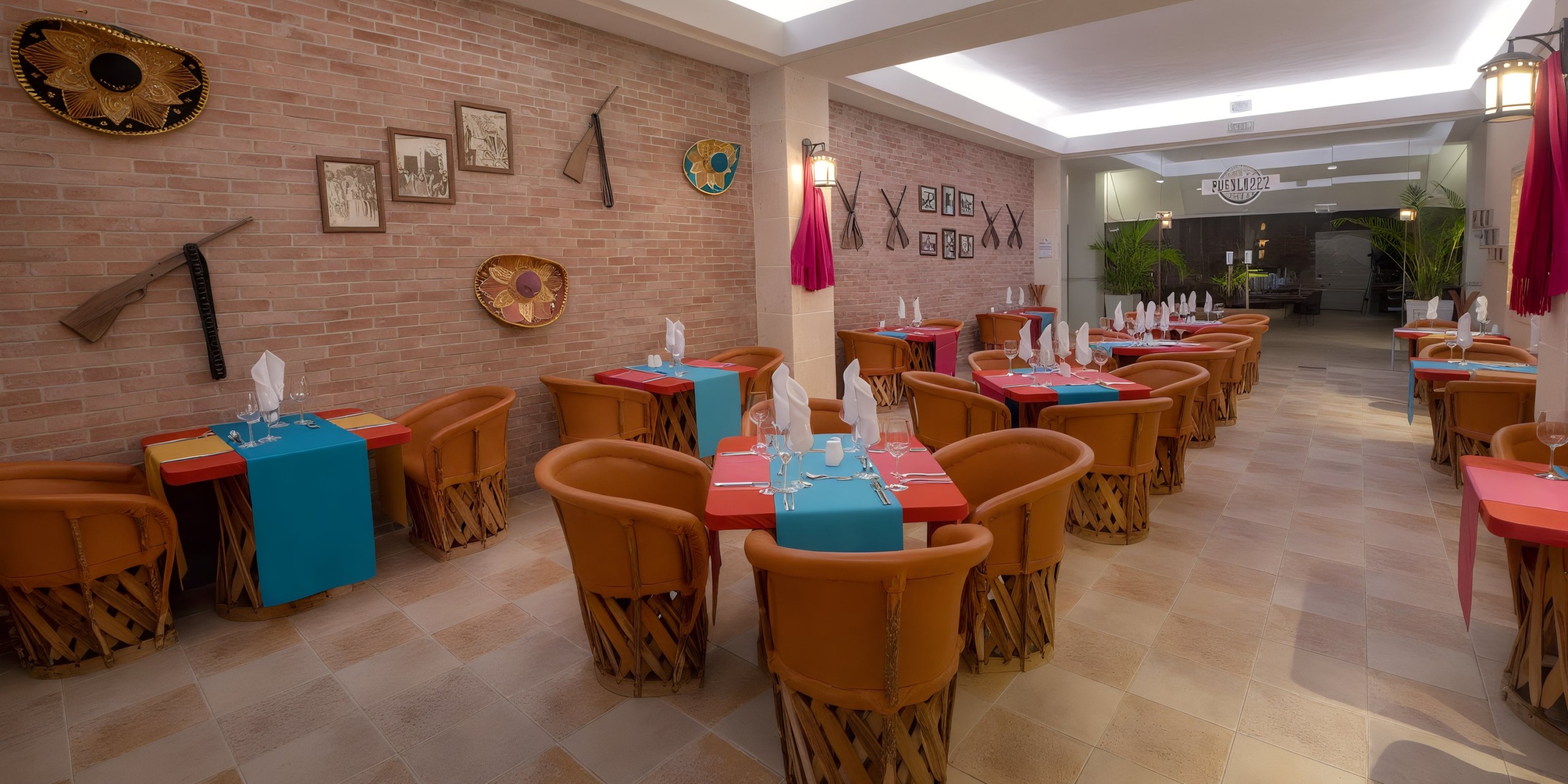 The restaurant interior at Viva Wyndham V Heavens - All-Inclusive Resort, Adults Only, features brick walls adorned with sombreros and framed pictures. Tables are elegantly set with red and teal tablecloths, complemented by woven leather chairs.