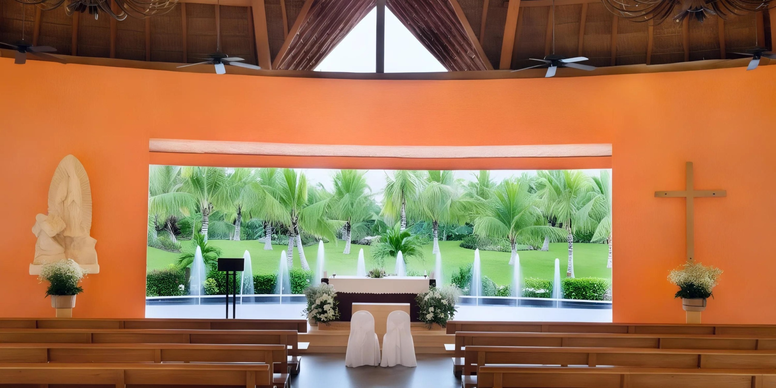 The Barcelo Maya Riviera boasts an intimate chapel interior with wooden benches arranged toward the altar. A large window frames a picturesque view of palm trees and lush greenery, while the orange walls are adorned with religious statues and a prominent cross.