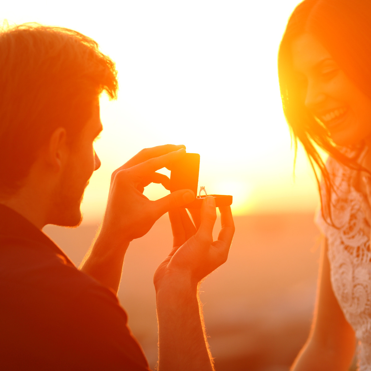 A man proposing to a woman at sunset, holding a ring, both bathed in golden light. This unique proposal idea creates a memorable moment.