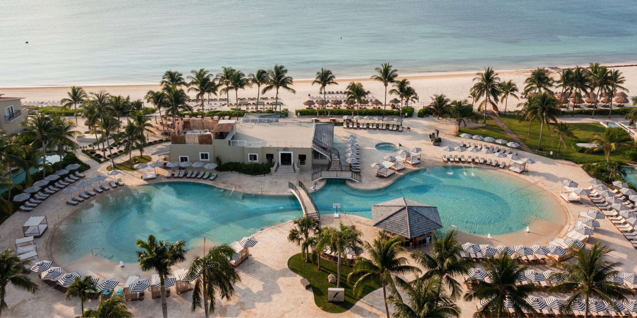 Aerial view of the Hyatt Zilara Riviera Maya, a beachfront resort featuring two round pools, numerous lounge chairs surrounded by palm trees, and a sandy beach that leads to calm ocean waters.