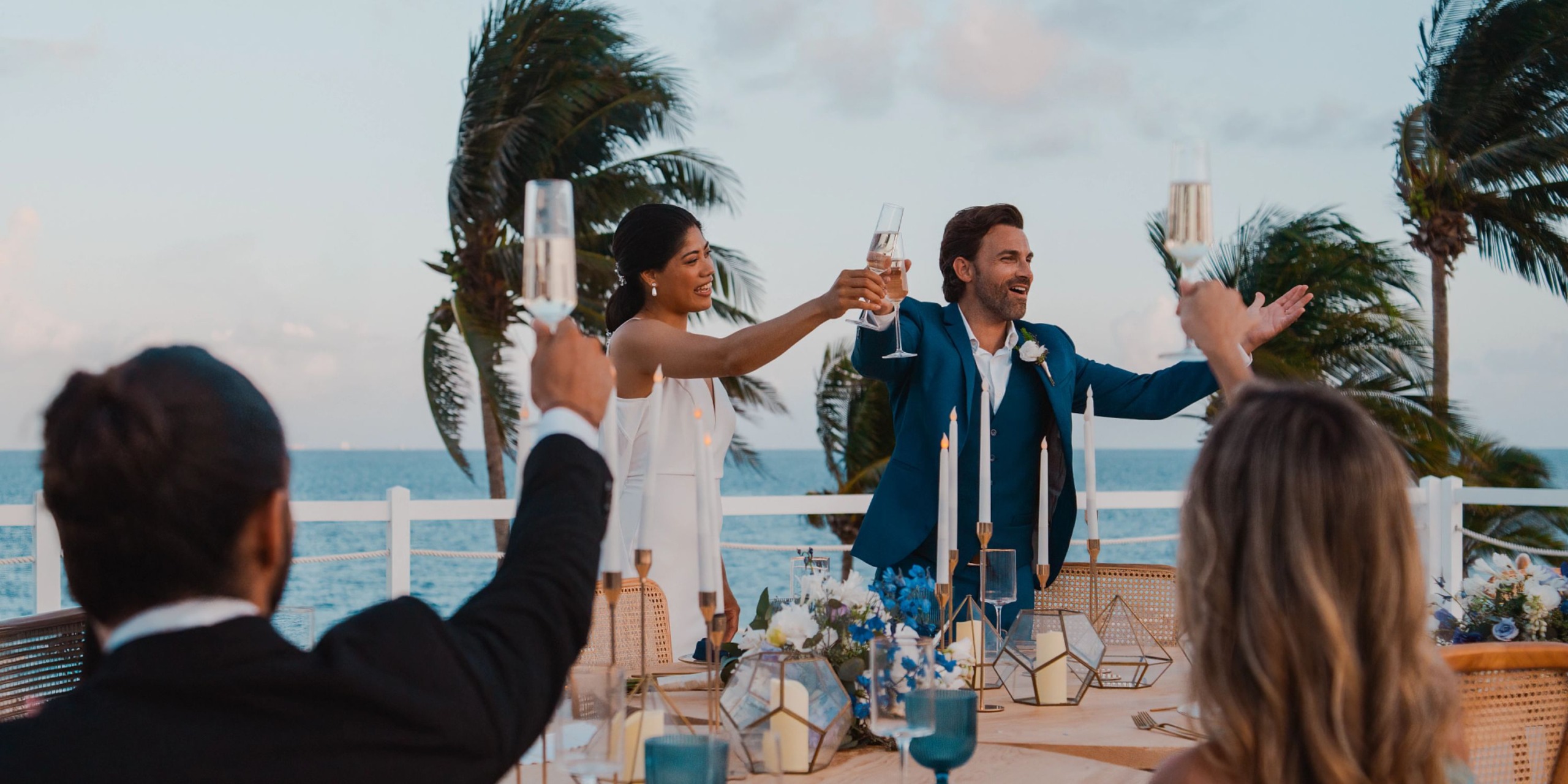 A couple in formal attire toasts with friends at an outdoor event by the ocean at Hyatt Zilara Riviera Maya.