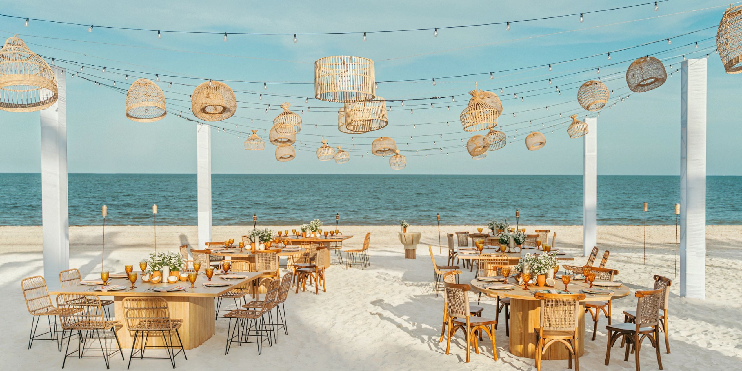 Enjoy a beachfront dining experience at Hyatt Zilara Riviera Maya, featuring wooden tables and chairs with overhead woven lanterns, all set against a stunning sea backdrop.