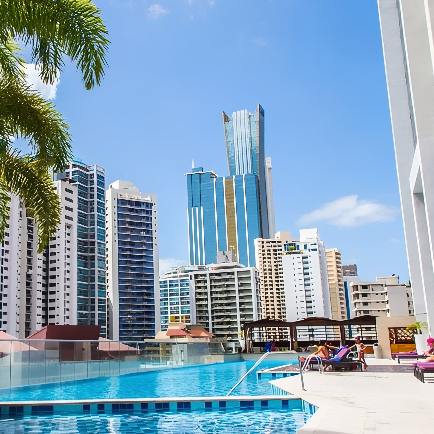 A rooftop pool with lounge chairs overlooks Hard Rock Panama Megapolis under a clear blue sky.