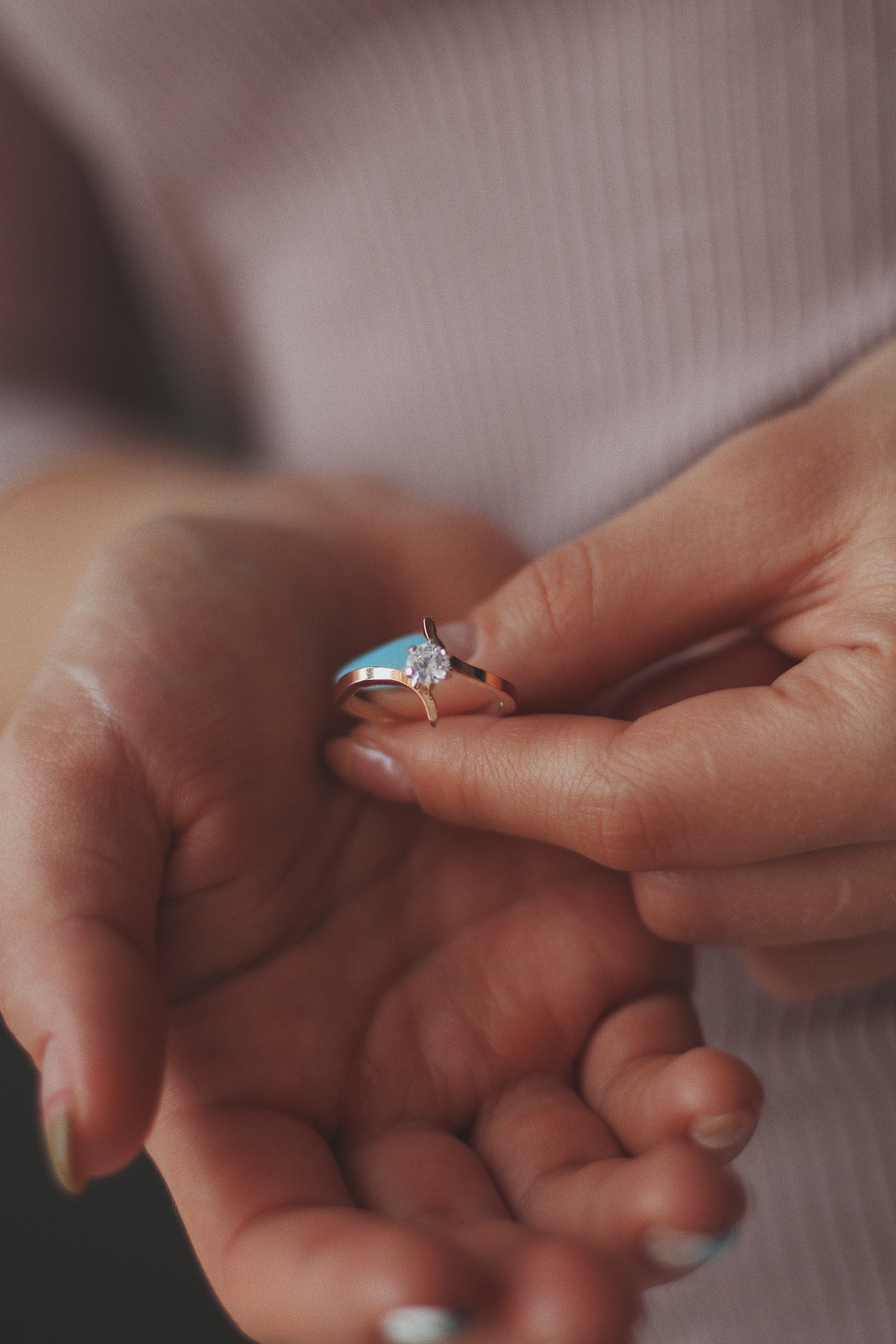 A person delicately holds a gold lab-grown diamond ring between their thumb and finger, perhaps envisioning it as the perfect choice for a wedding or even a dream destination wedding.