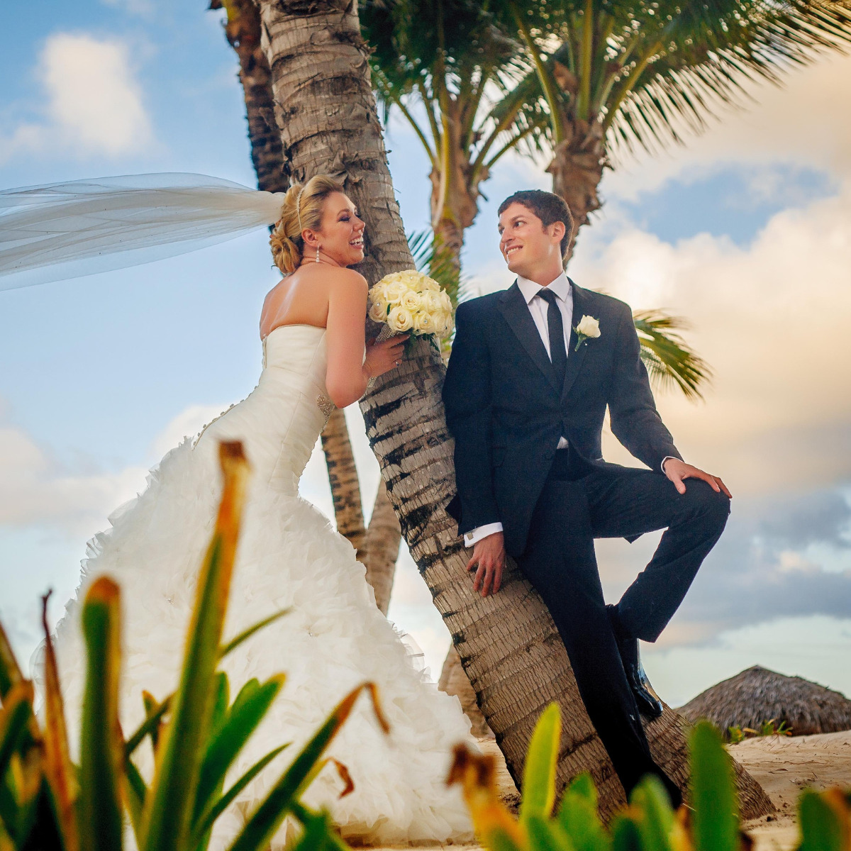 A couple leans against a palm tree after their destination wedding using a Caribbean Islands Wedding Package Under $5000
