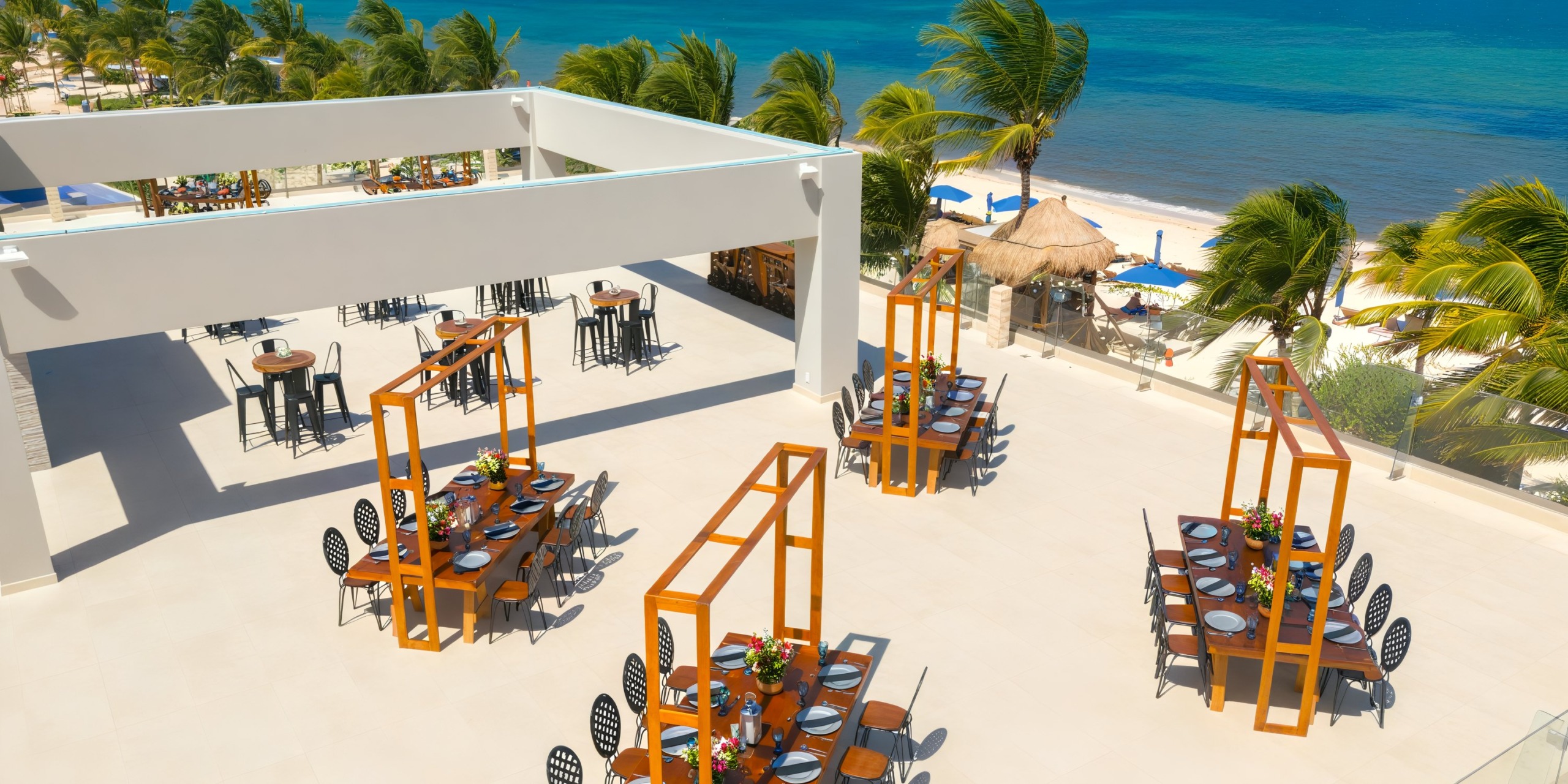 Royalton Splash Riviera Cancun: The perfect destination wedding venue featuring beachfront dining with wooden tables and chairs, all set among ocean-view palms.